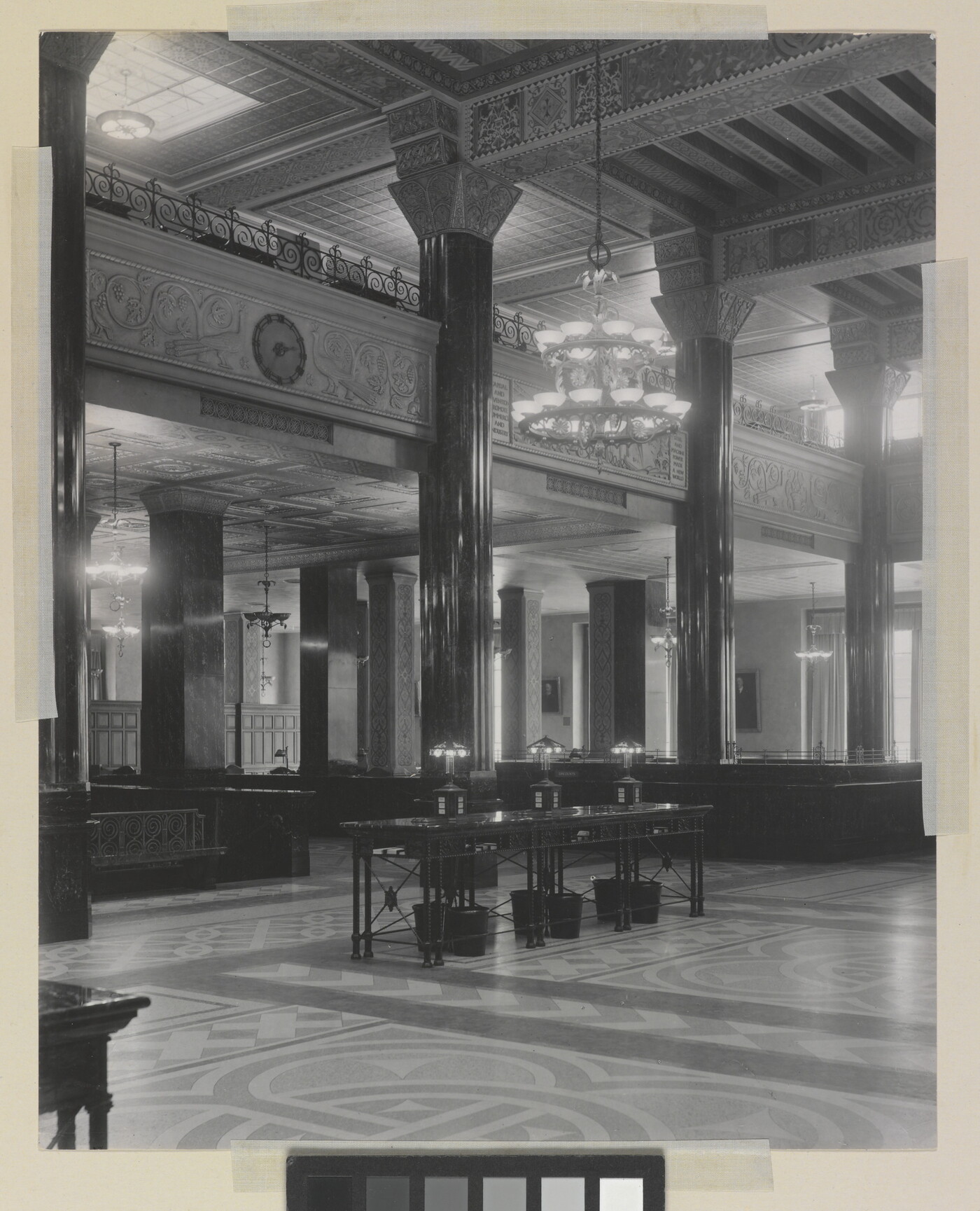 A black-and-white photograph of the interior of an ornate office lobby with inlaid floors, columns, and chandeliers.