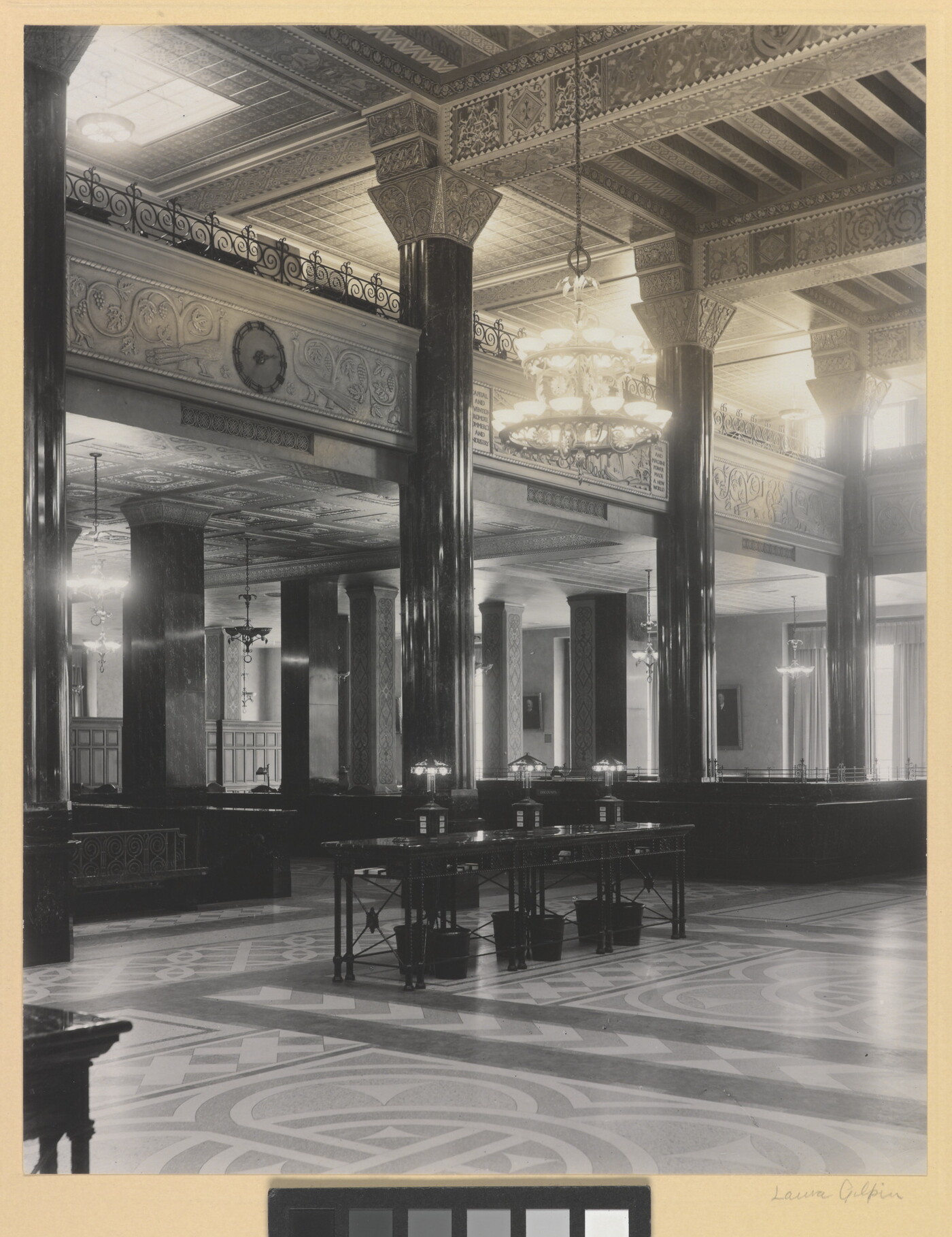 A black-and-white photograph of the interior of an ornate office lobby with inlaid floors, columns, and chandeliers.