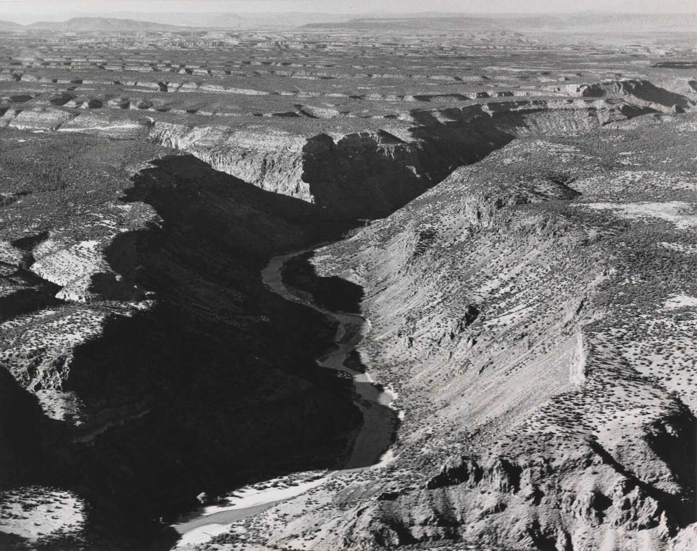 A black-and-white photograph of an aerial view of a river winding through a steep canyon.