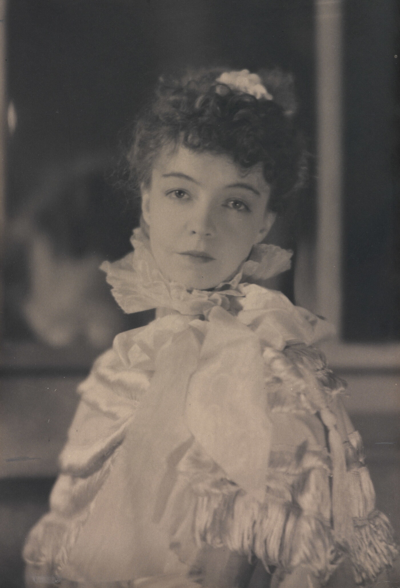 A black-and-white portrait photograph of a White woman with curly hair pulled on top of her head, wearing a top with a ruffled collar.