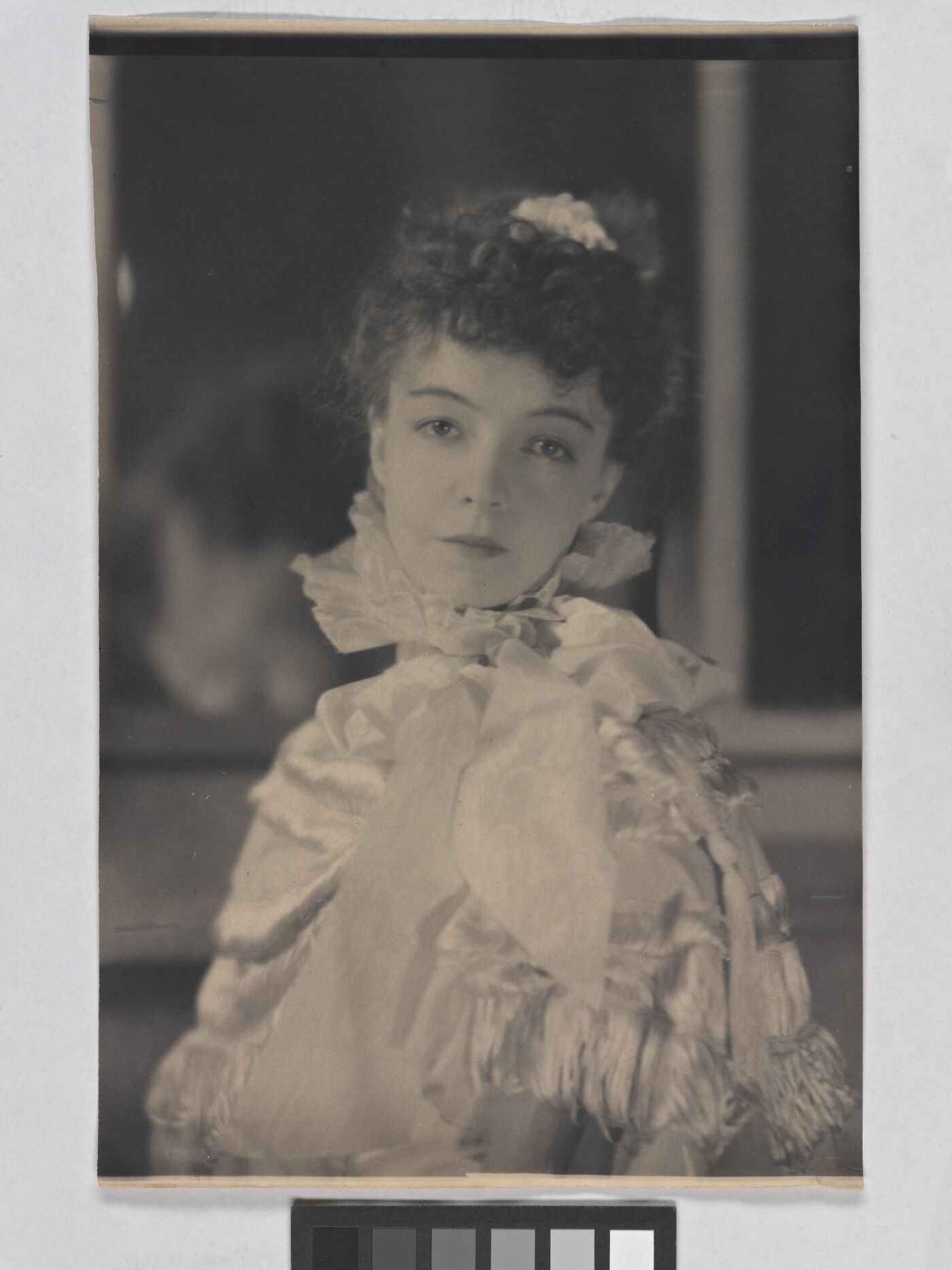 A black-and-white portrait photograph of a White woman with curly hair pulled on top of her head, wearing a top with a ruffled collar.