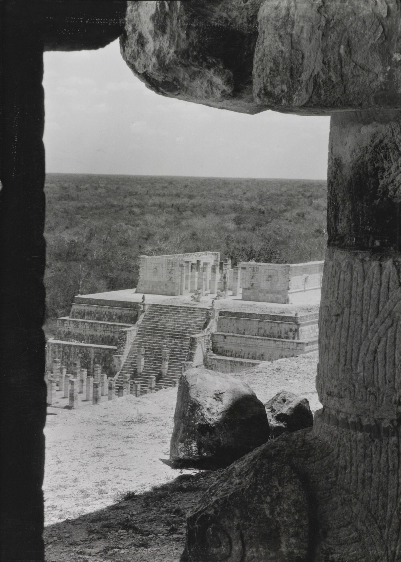 A black-and-white photograph of an ancient step pyramid viewed through a stone window.