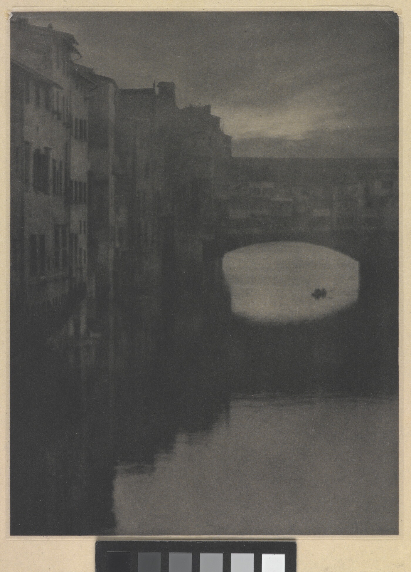 A sepia-toned photograph of a wall of tall buildings lining a river and an enclosed arched bridge stretching over the water.