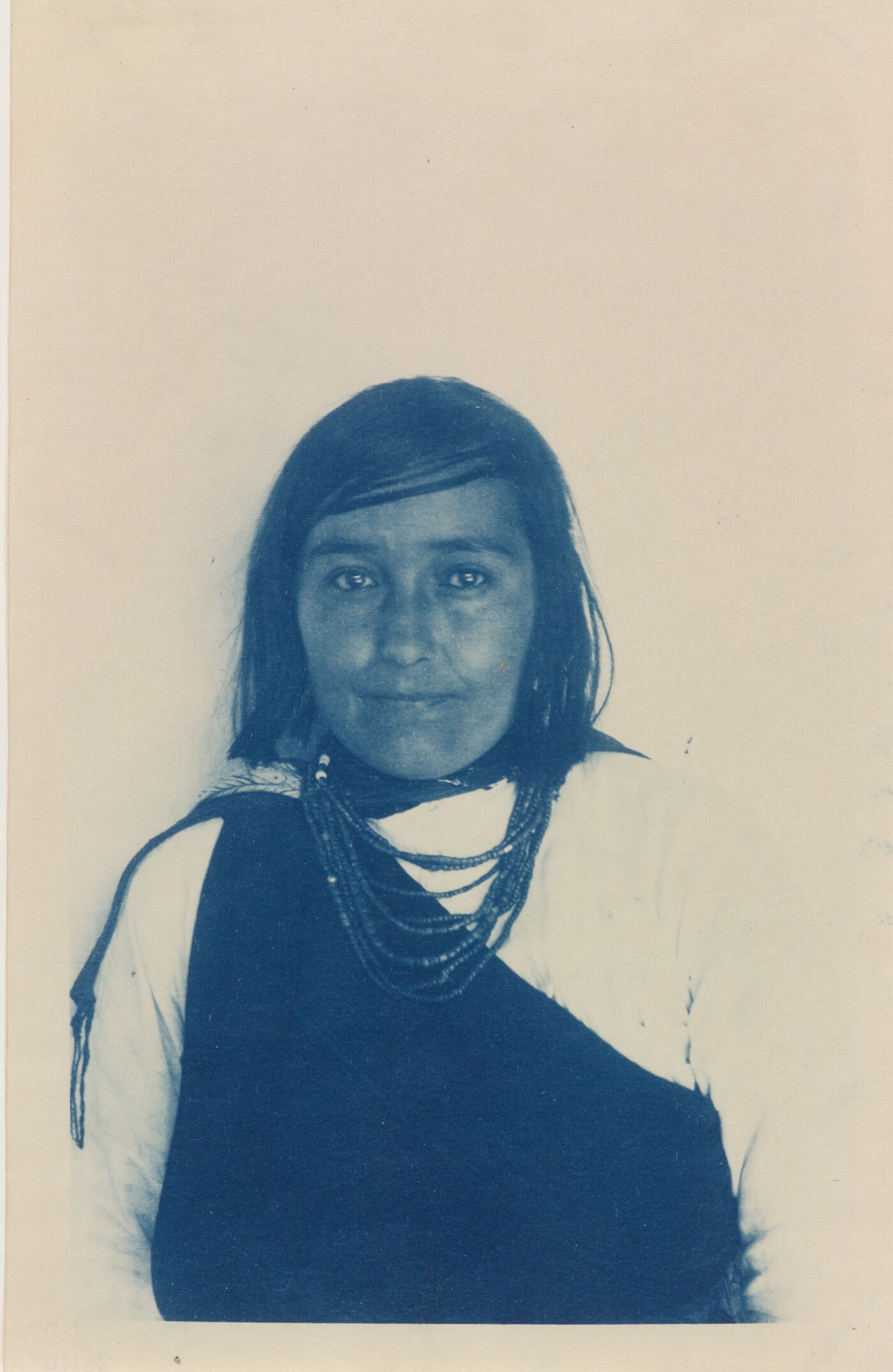 A blue-tinted black-and-white portrait photograph of a young American Indian woman wearing a multi-strand necklace.