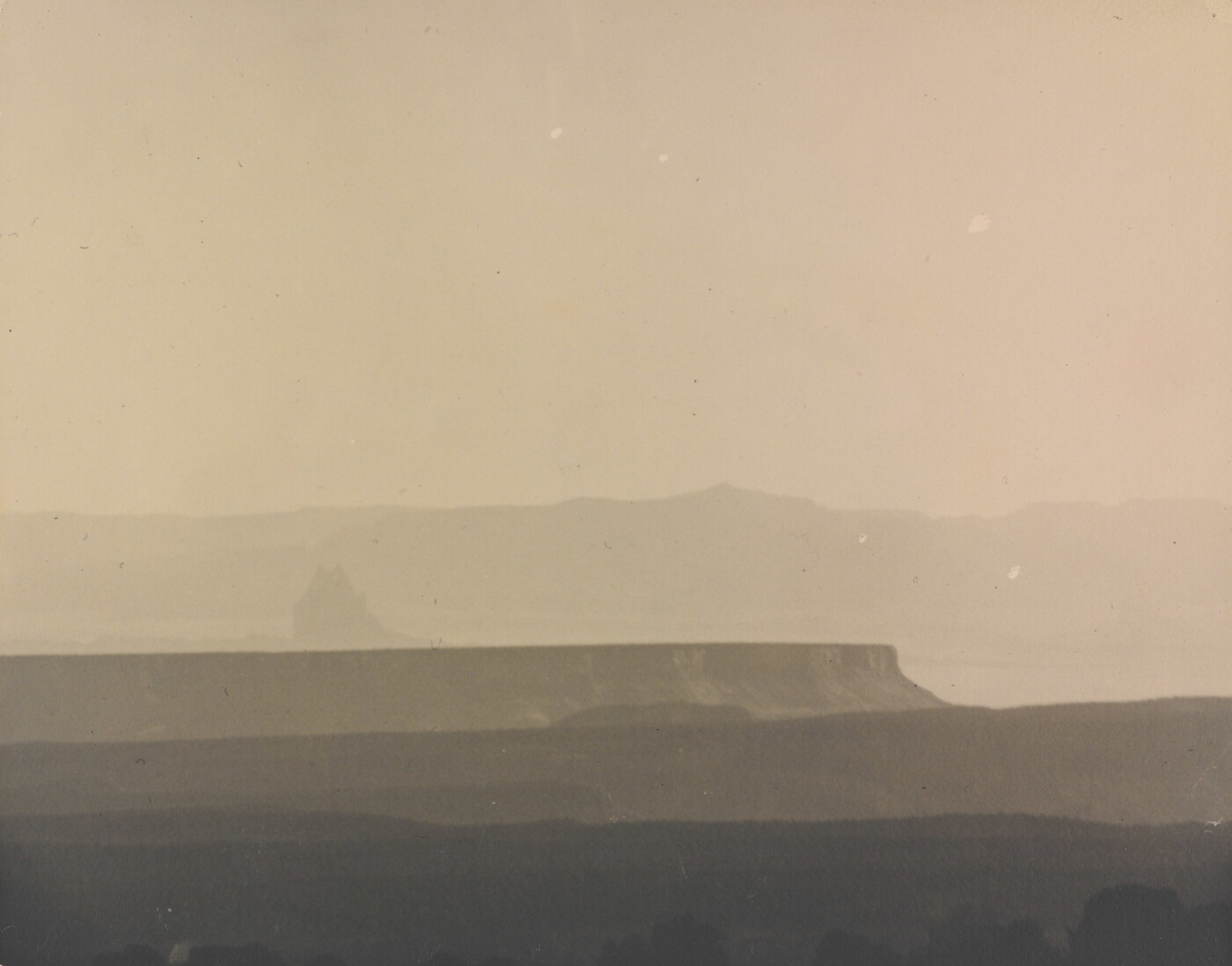 A sepia-toned photograph of a hazy mesa and distant mountains.
