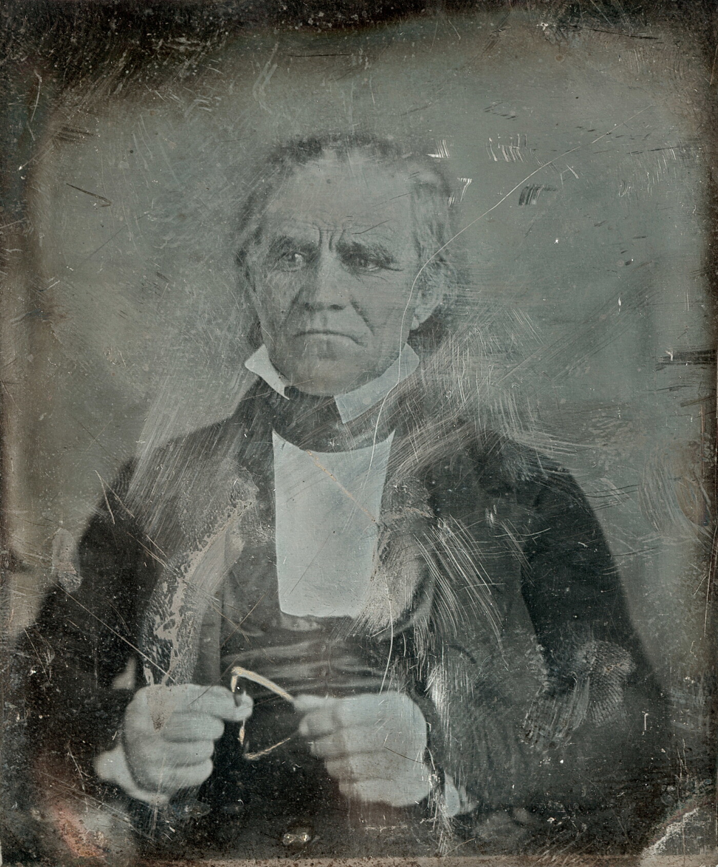 A worn and scratched black-and-white photograph of a seated, older White man in a suit.
