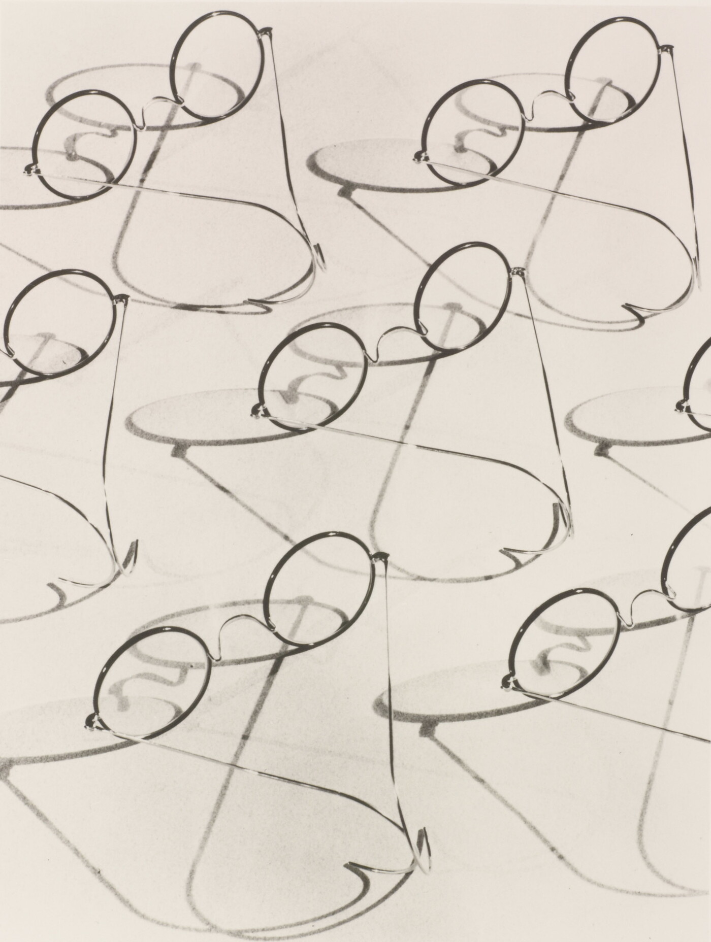 A black-and-white photograph of multiple granny-style eyeglasses and their shadows.
