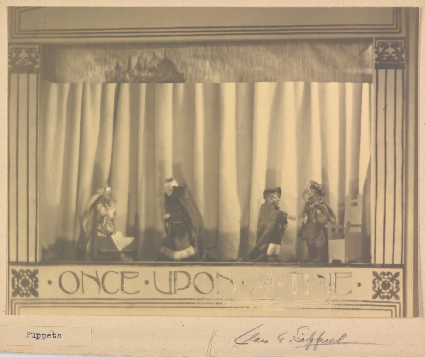 A sepia-toned photograph of a puppet stage with four puppets and the words &quot;Once Upon a Time&quot; written at the bottom.