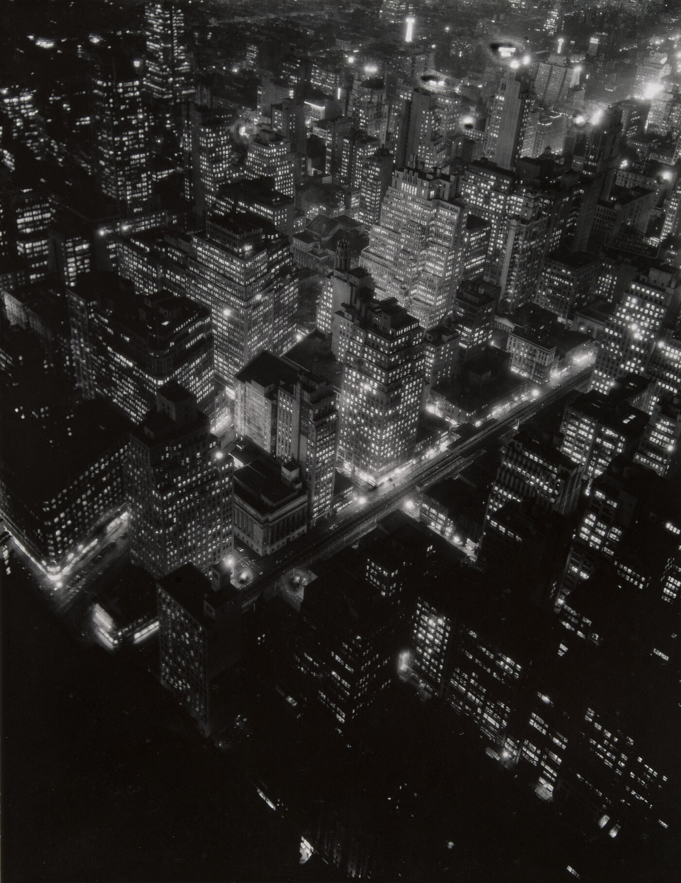 A black-and-white photograph of a bird&#039;s eye view of city lights at night.