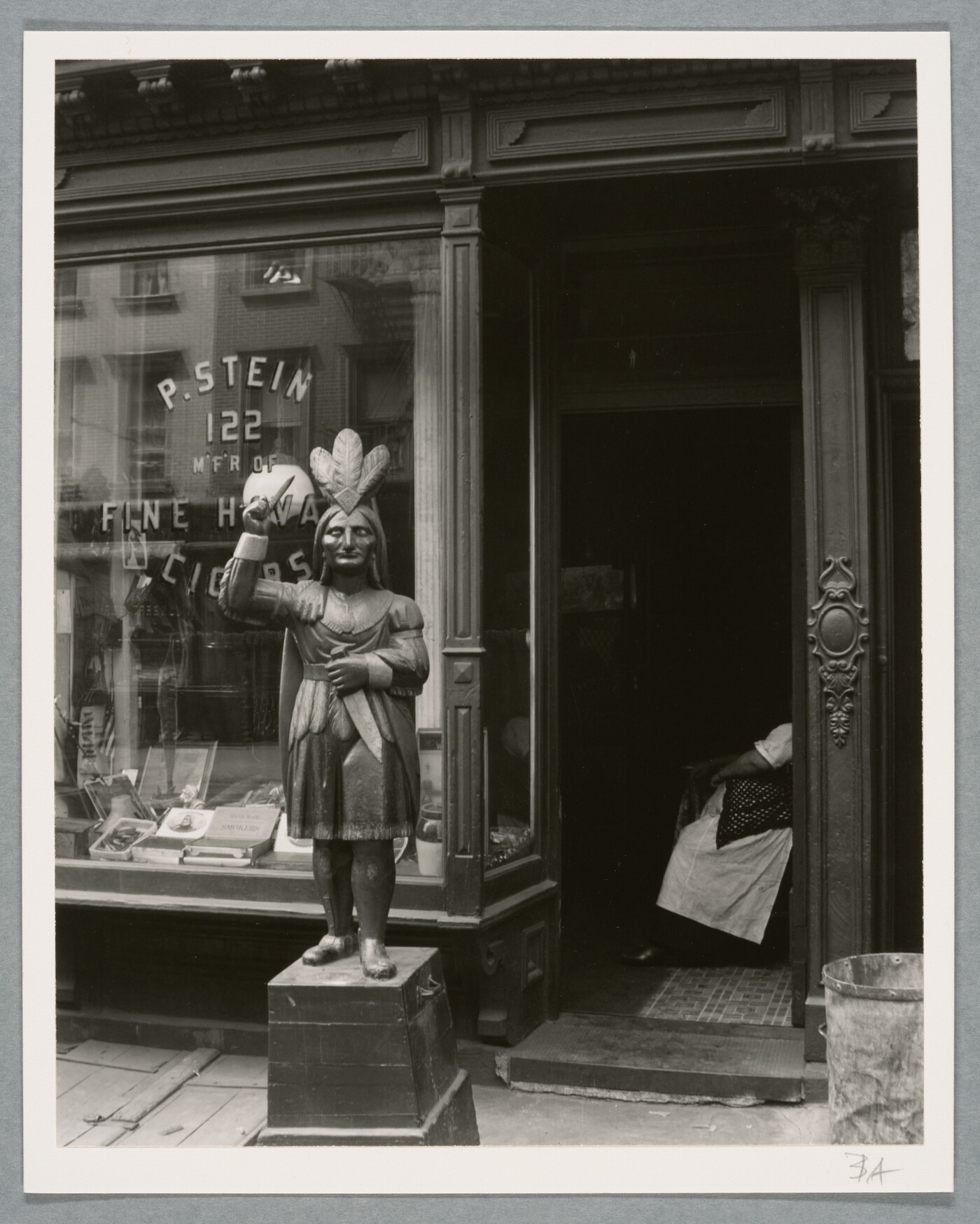 A black-and-white photograph of a storefront with a statue of an Indigenous person at the entrance.