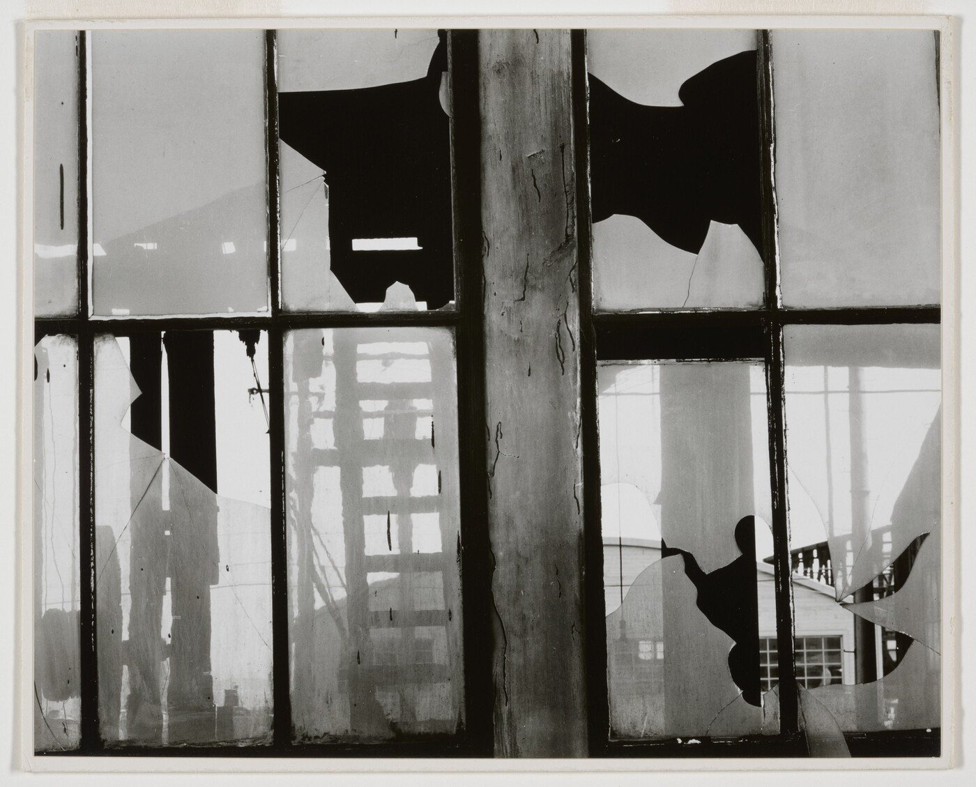 A black-and-white photograph of broken window panes in what looks like a factory building.