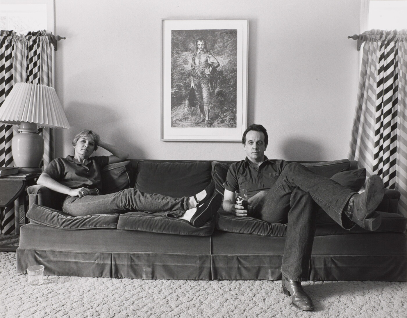 A black-and-white photograph of a woman and a man seated at opposite ends of a couch.