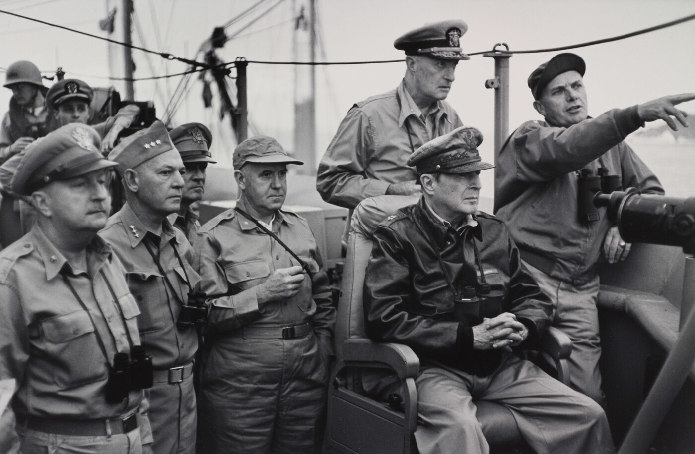 A black-and-white photograph of White men in military uniforms, binoculars hanging around their necks, looking in the direction one of the men is pointing.