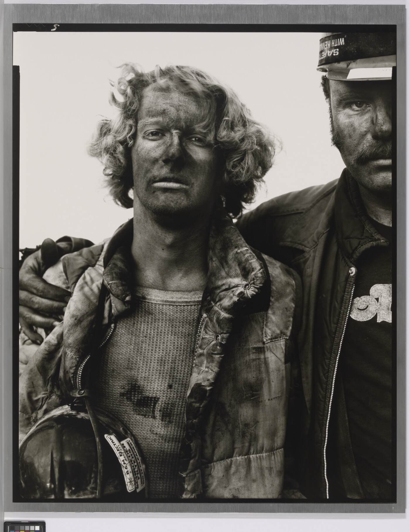 A black-and-white portrait photograph of two men, one with his arm around the other, both covered in coal dust and wearing dirty clothes.