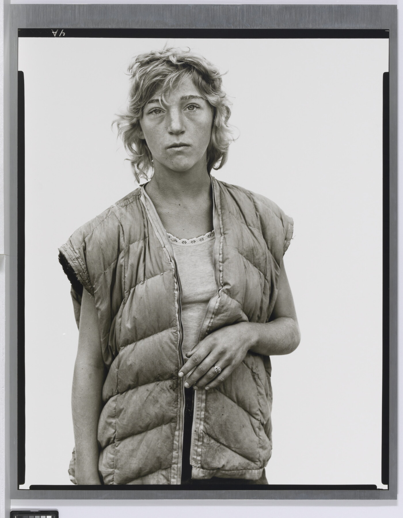 A black-and-white portrait photograph of a young White woman with short wavy hair wearing a puffer vest looking straight at the viewer.