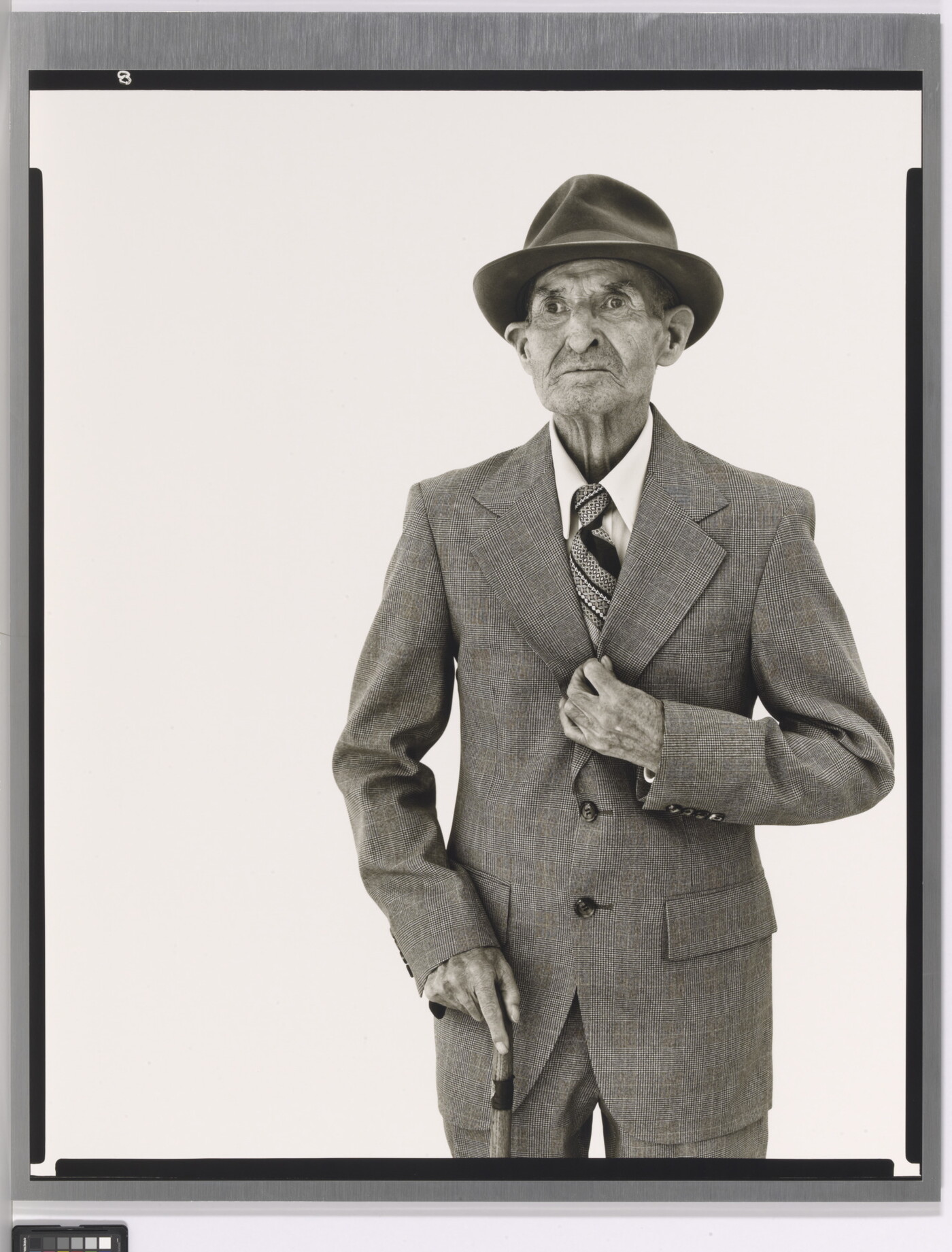 A black-and-white portrait photograph of an elderly White man in a hat, suit, tie, and one hand holding a cane.