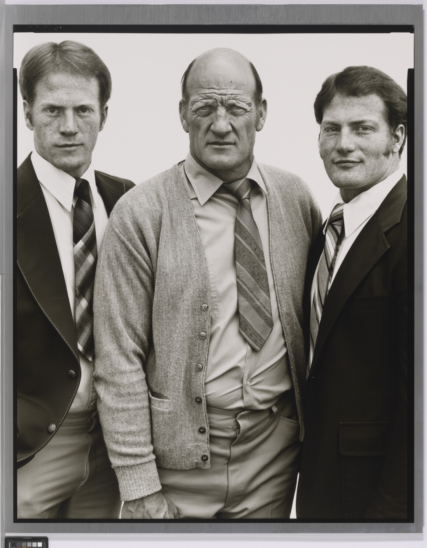 A black-and-white portrait photograph of three White men, two younger on the left and right and the one in the center middle-aged and bald, all wearing suits and ties.