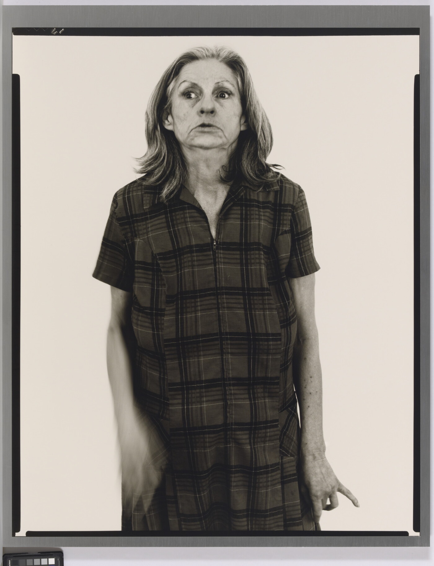 A black-and-white portrait photograph of an older White woman with medium-length gray hair, head held back slightly, wearing a house dress.