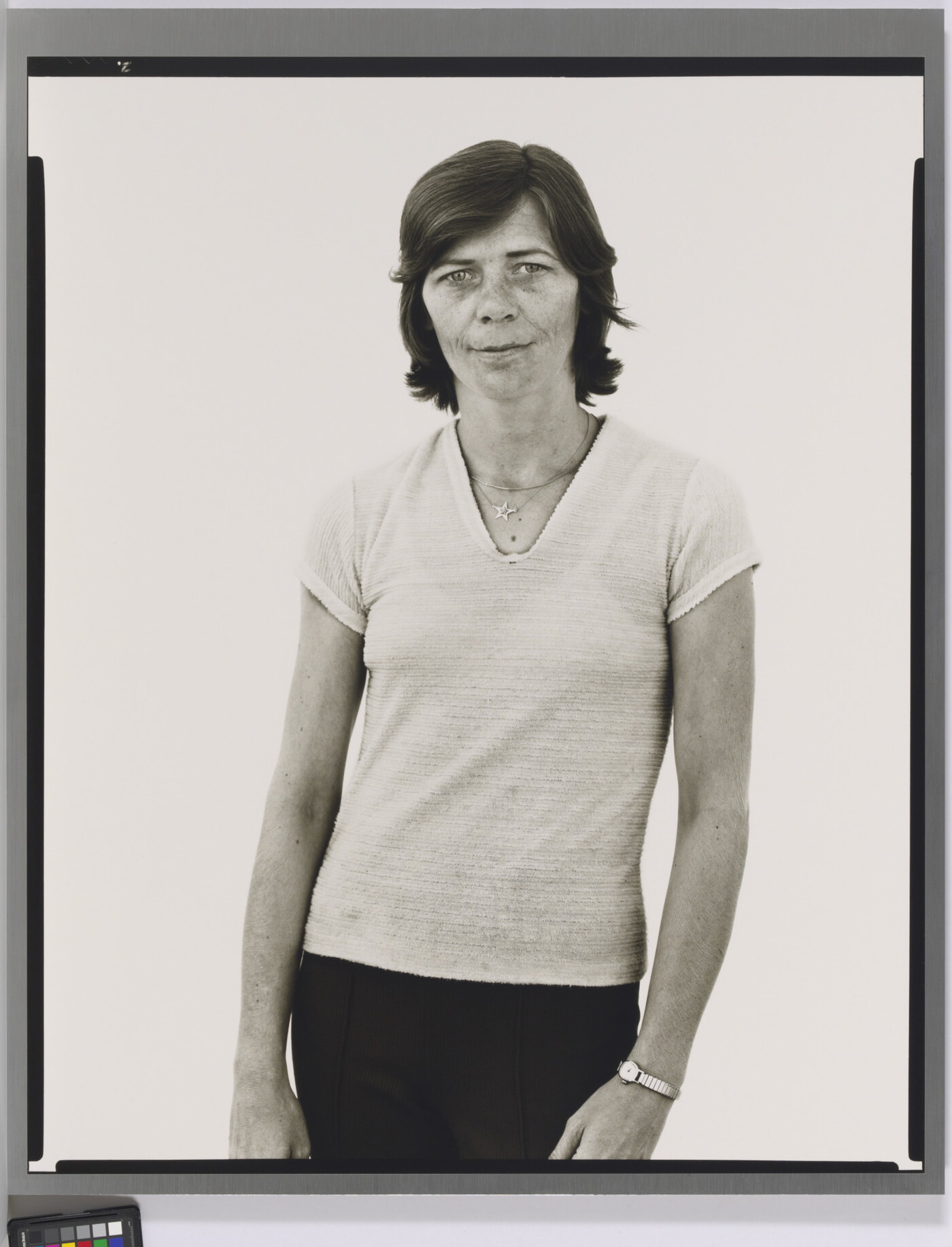 A black-and-white portrait photograph of a White woman with short hair, wearing a light V-neck shirt and dark pants.