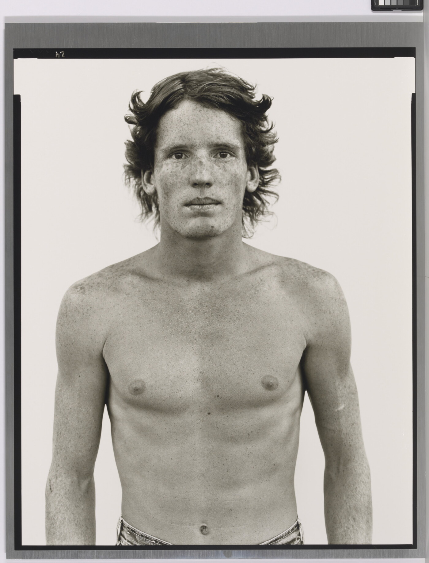 A black-and-white portrait photograph of a shirtless young White man with freckles across his face and shoulders.