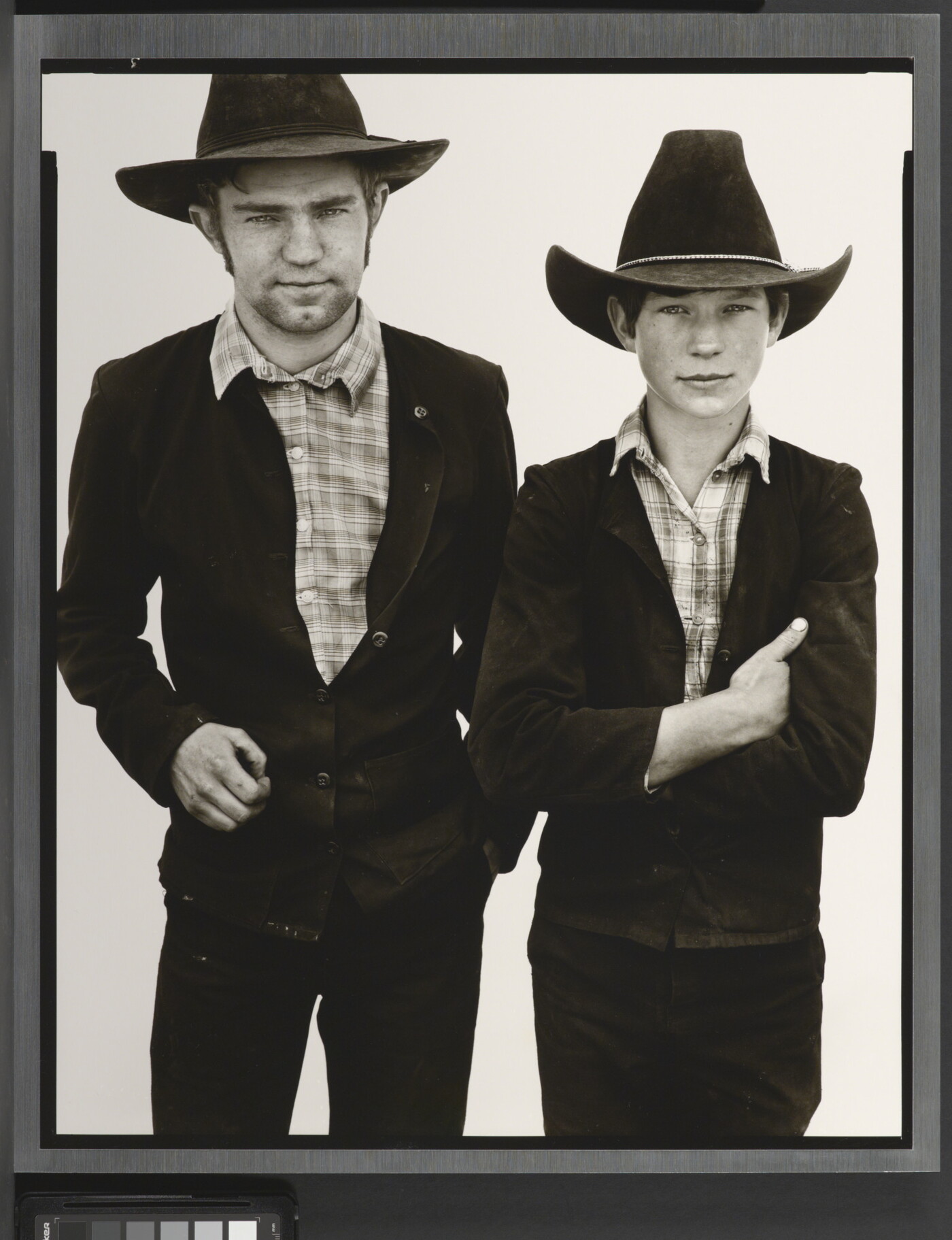 A black-and-white portrait photograph of a young White man and boy, both wearing cowboy hats, dark jackets, and plaid shirts.