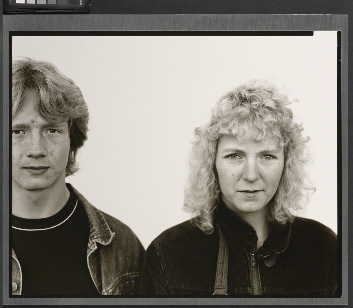 A black-and-white portrait photograph of a young White man with shaggy hair wearing a jean jacket, and a young White woman with curly hair wearing a corduroy jacket.