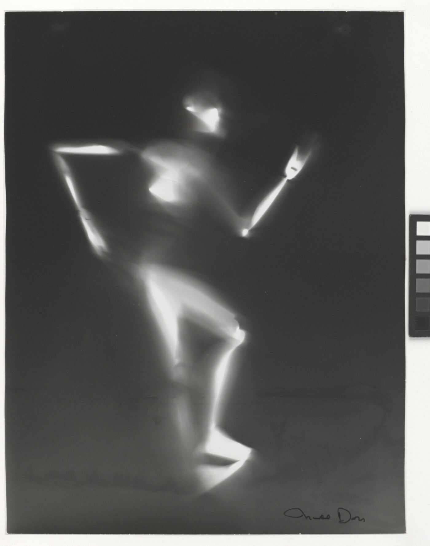 A black-and-white photograph of a white person-shaped puppet dancing on a black background.