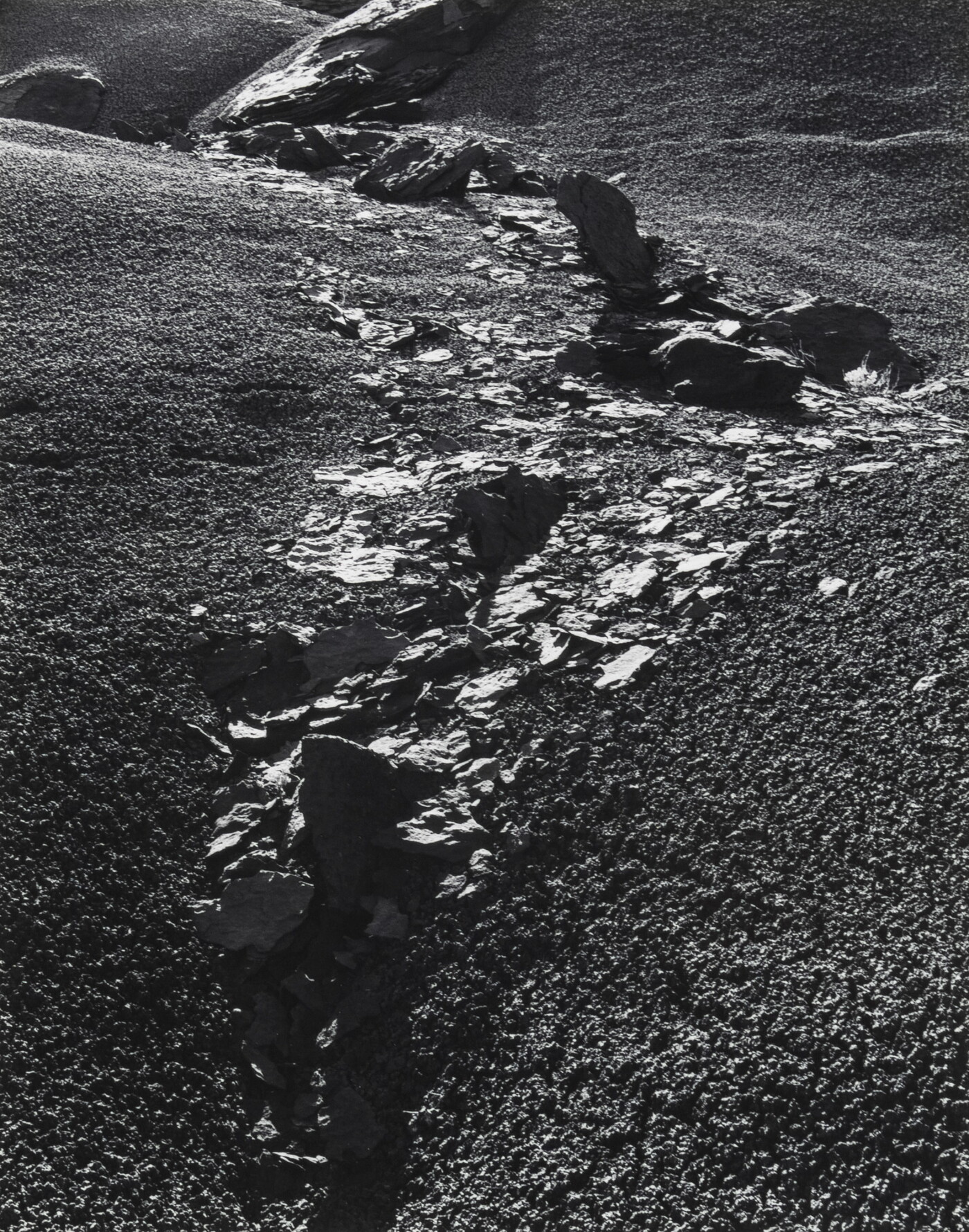 A black-and-white photograph of rocks and rock flakes bisecting a gravelly slope.