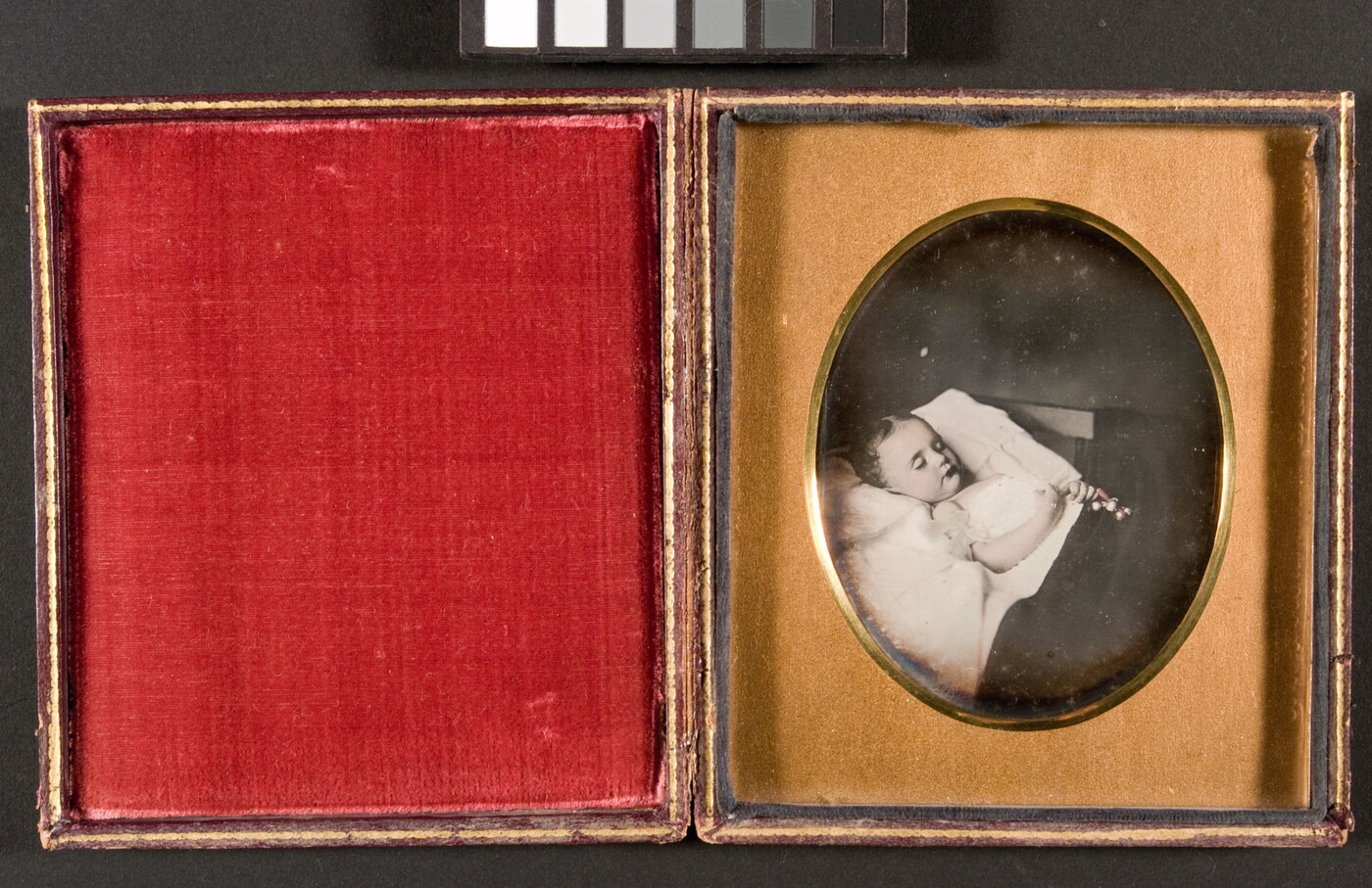 A black-and-white photograph in a gold frame of a child with closed eyes laying in bed with a toy in her clasped hands.