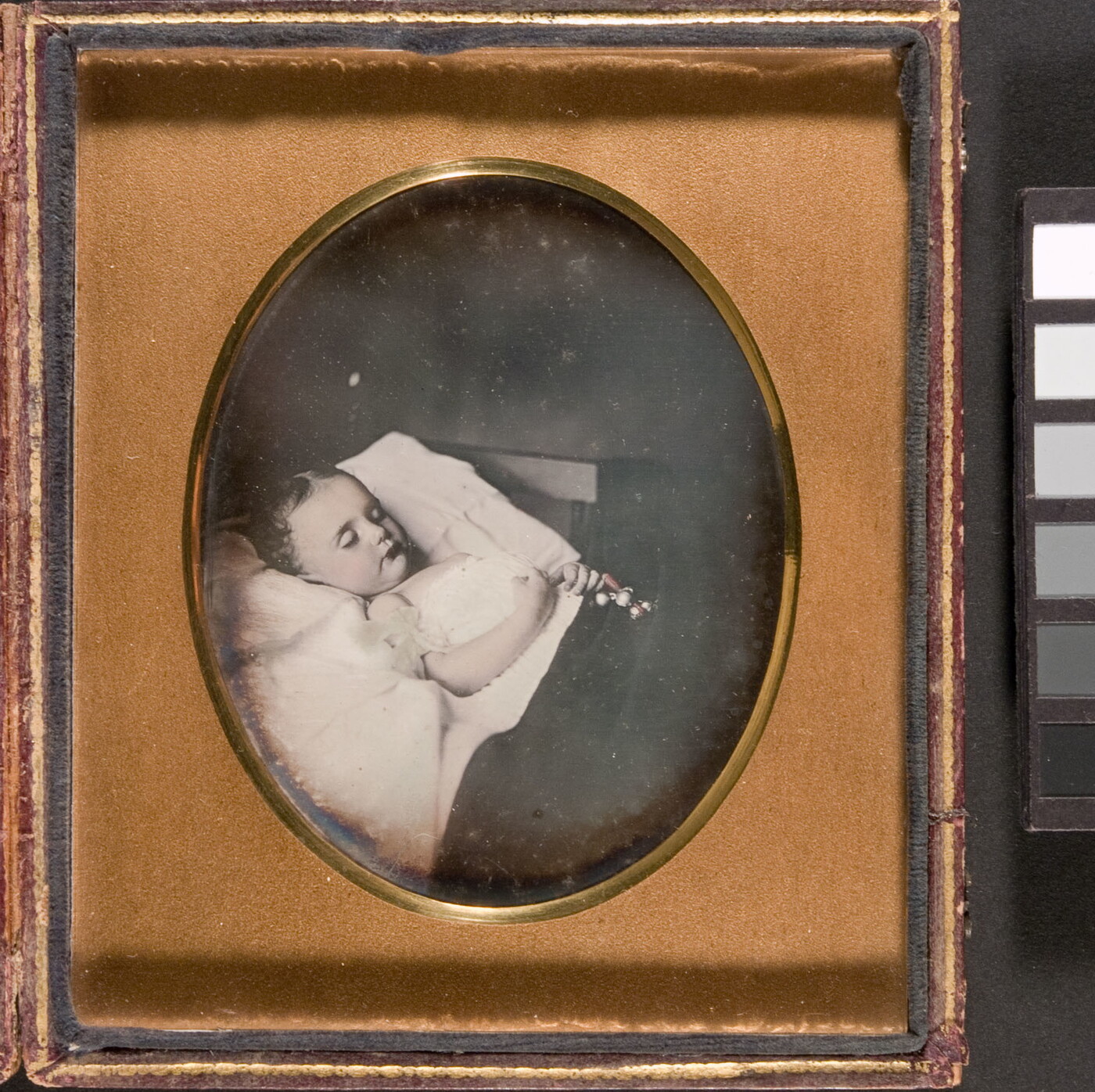 A black-and-white photograph in a gold frame of a child with closed eyes laying in bed with a toy in her clasped hands.