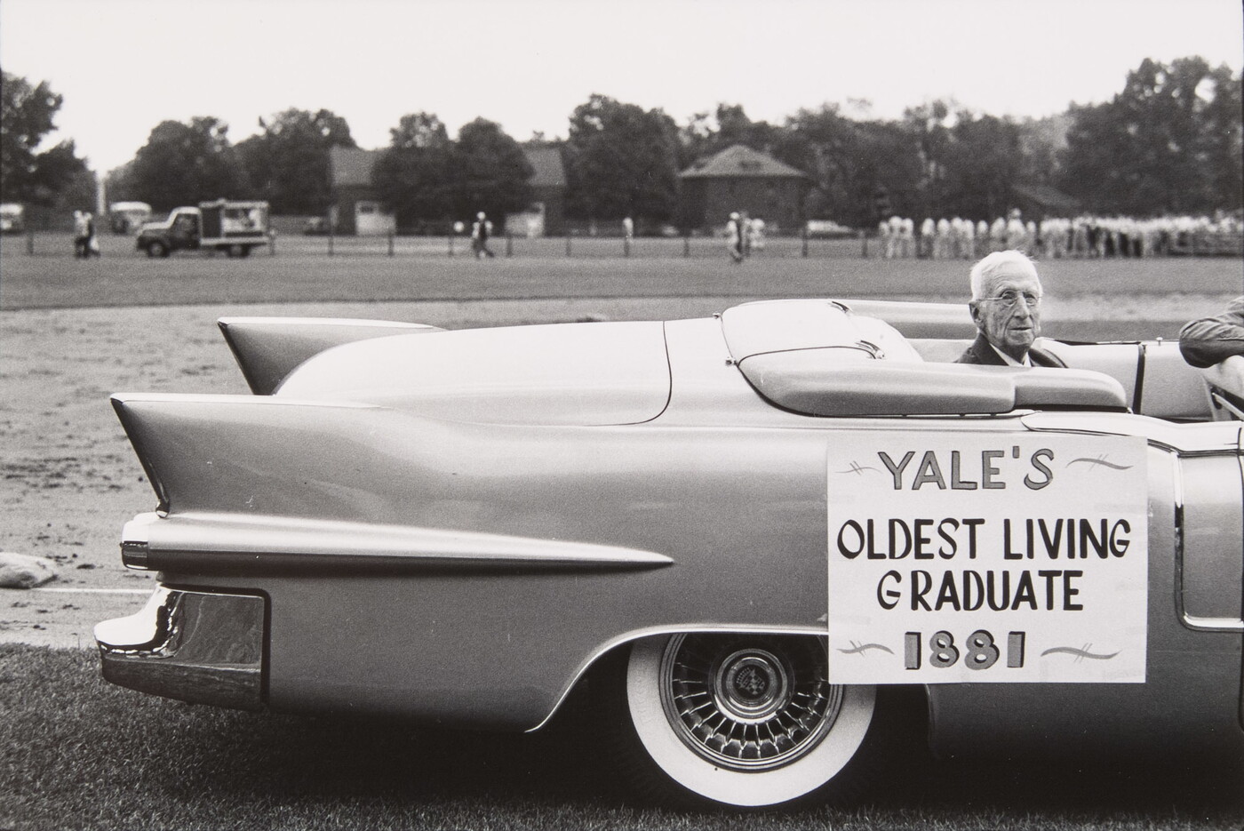 A black-and-white photograph of an elderly White man seated in the back of a convertible; a sign on the car reads, &quot;Yale&#039;s oldest living graduate, 1881.&quot;