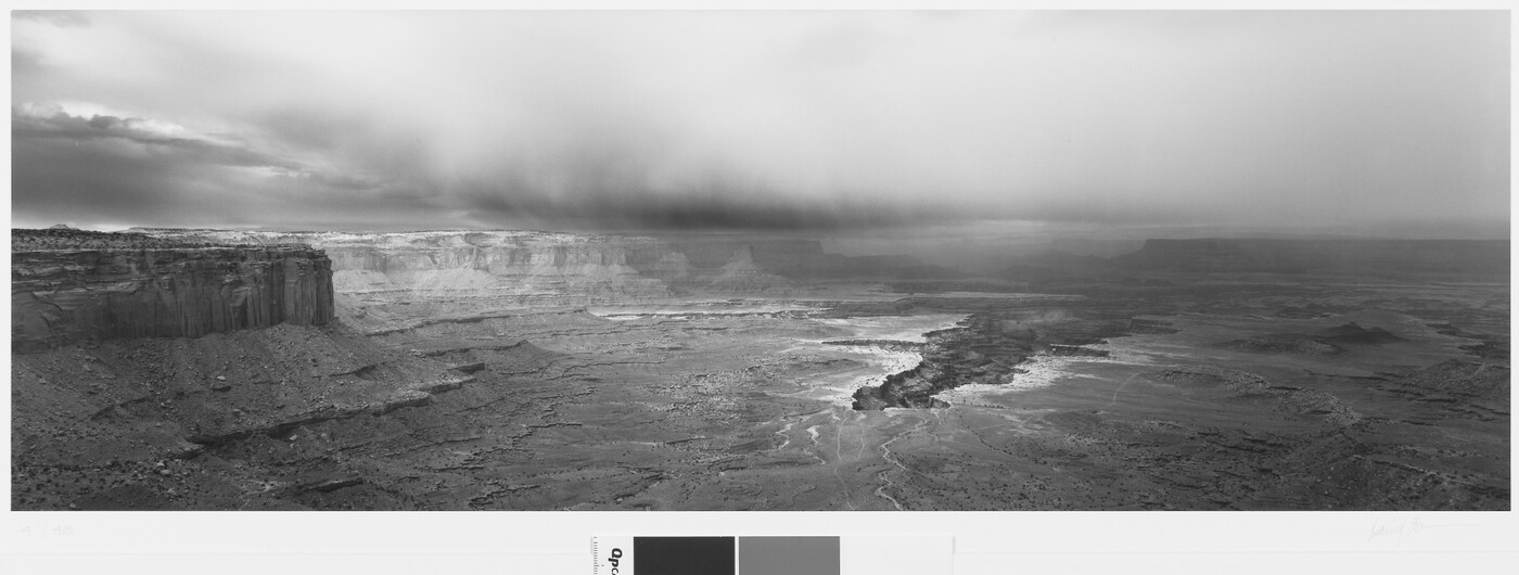 A black-and-white panoramic photograph of a steep canyon under a stormy sky.