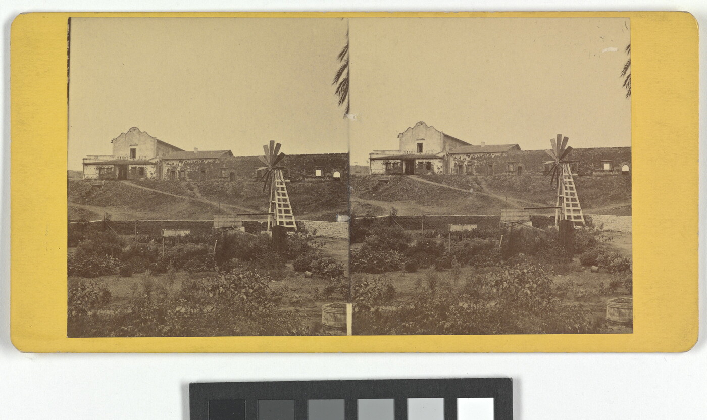 Two almost identical sepia-toned photographs side by side an adobe building on a hill with a windmill in the foreground.