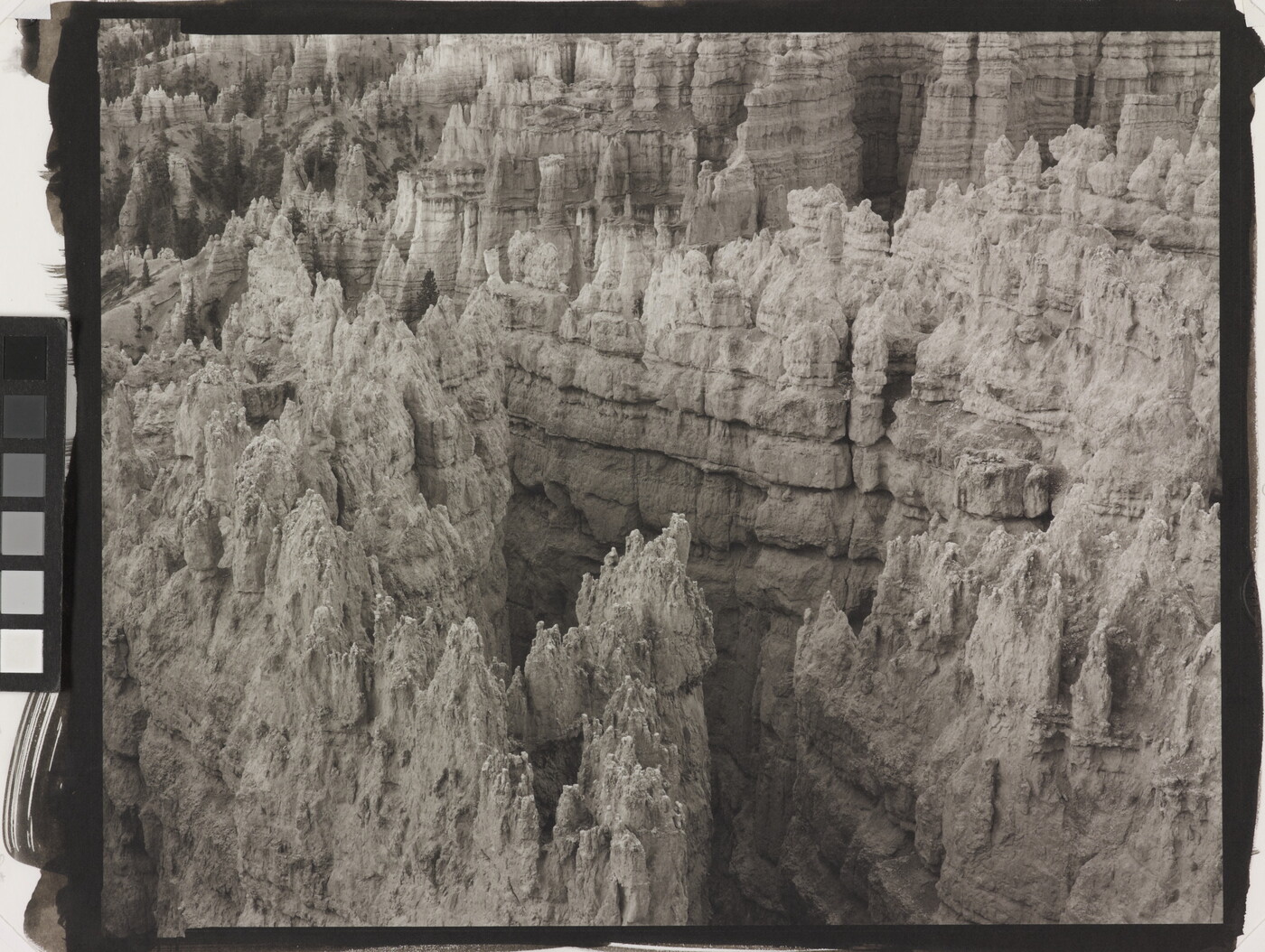A black-and-white landscape photograph of a view of banded rock formations in a canyon.