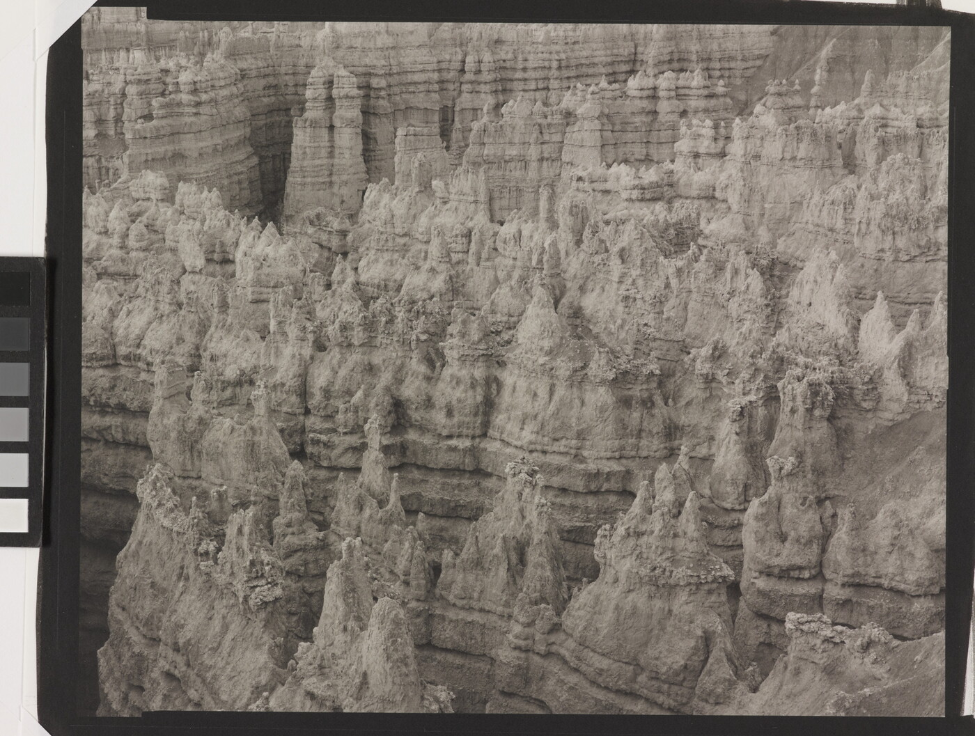 A black-and-white landscape photograph of a view of banded rock formations in a canyon.