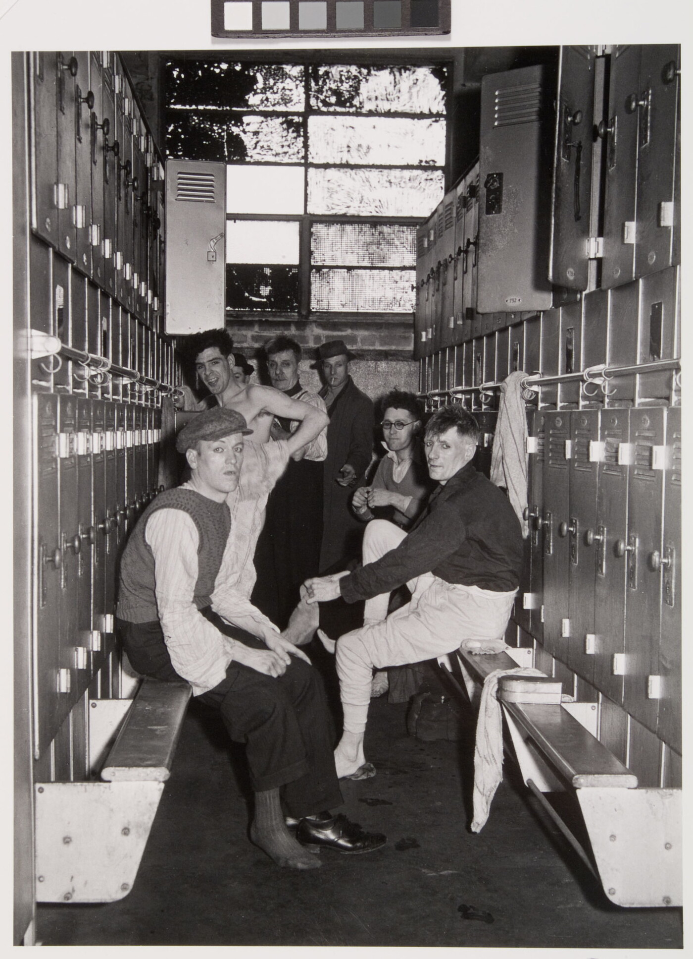 A black-and-white photograph of several men in various states of dress in the row of a locker room.