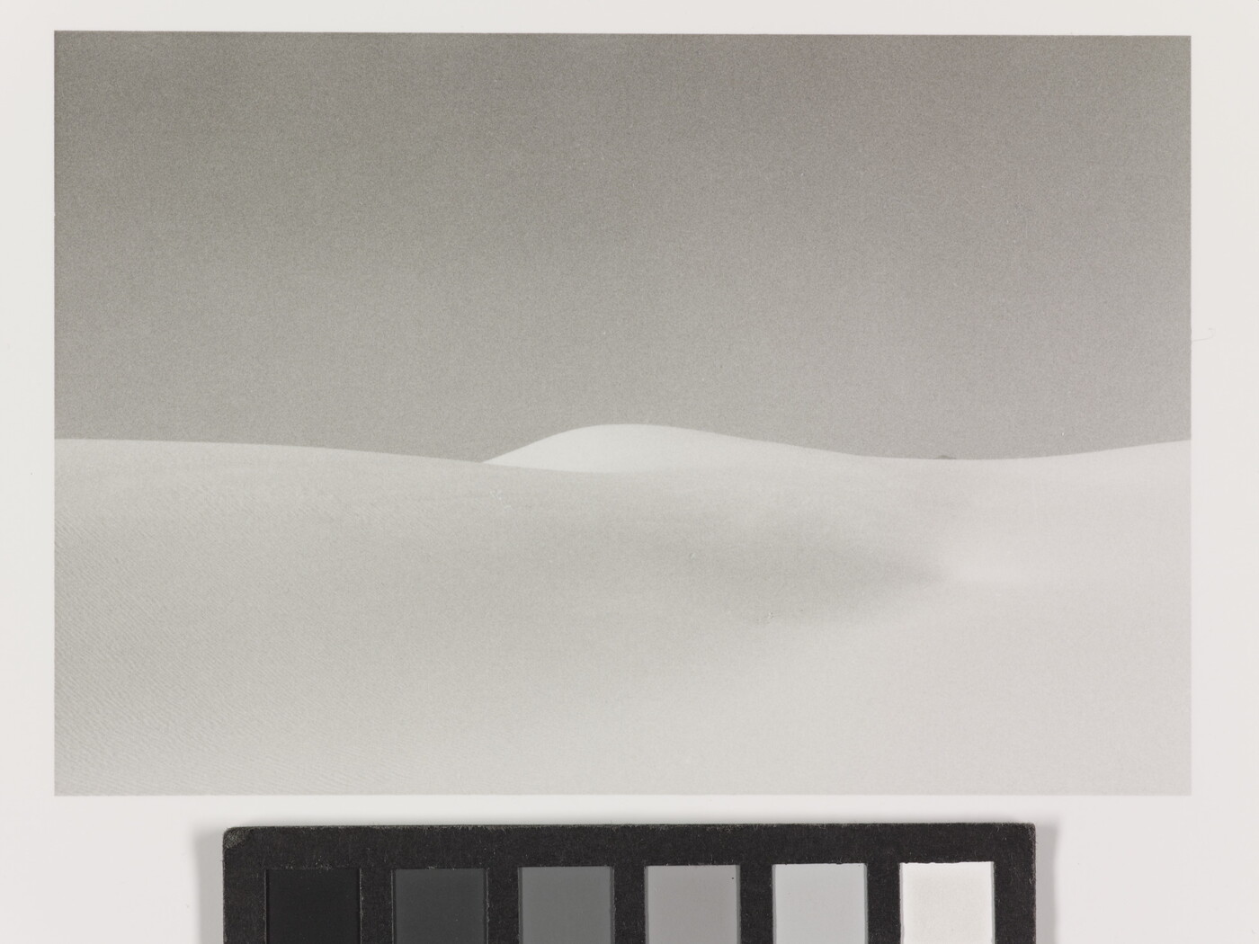 A black-and-white landscape photograph of a white sand dune against a gray sky.