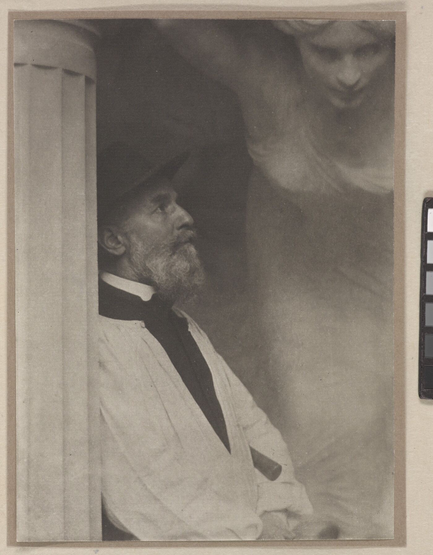 A black-and-white photograph of an older White man in profile leaning against a fluted column with what looks like a sculpture of a woman hovering over him.