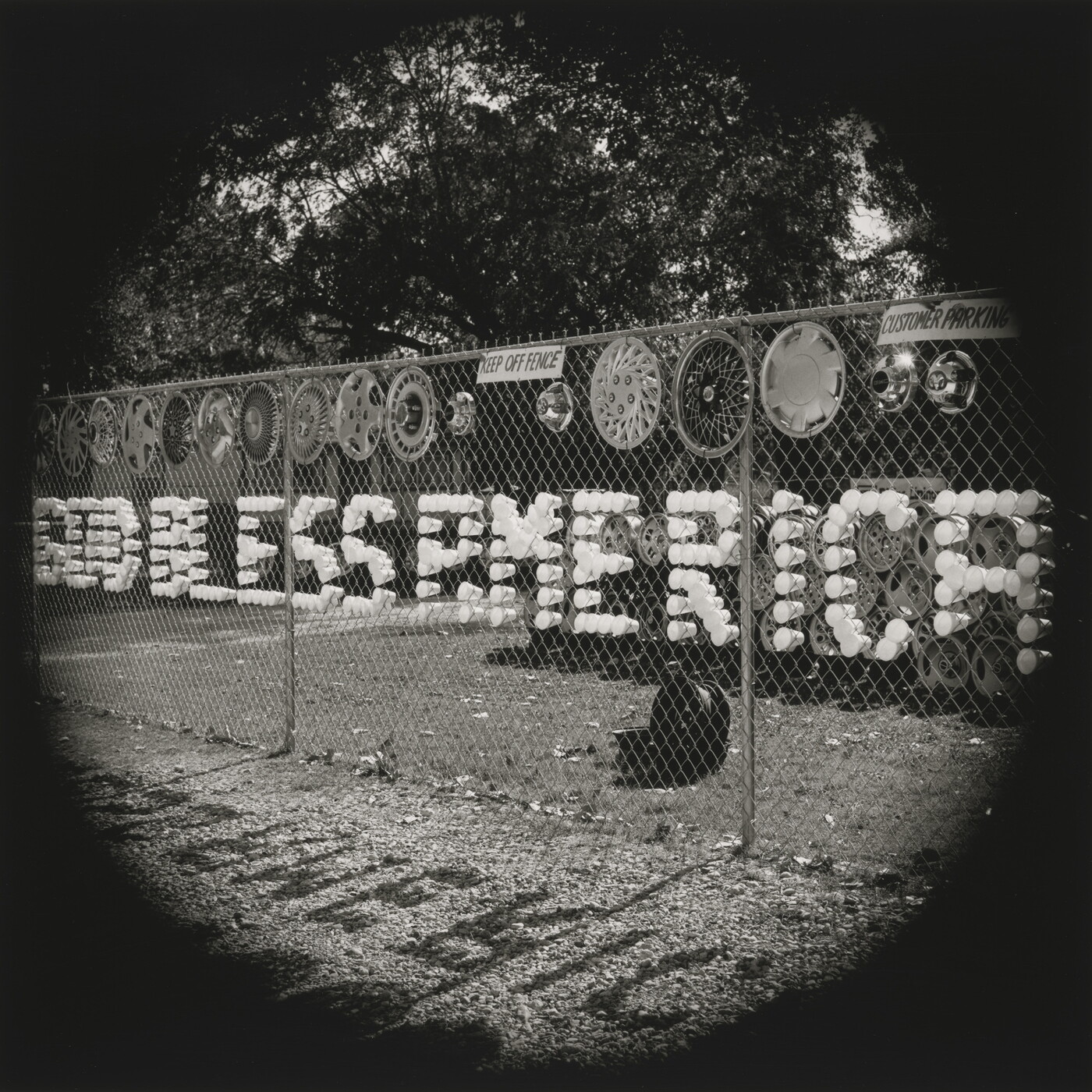A black-and-white photograph of plastic cups arranged in a chain-link fence to spell out &quot;God Bless America.&quot;