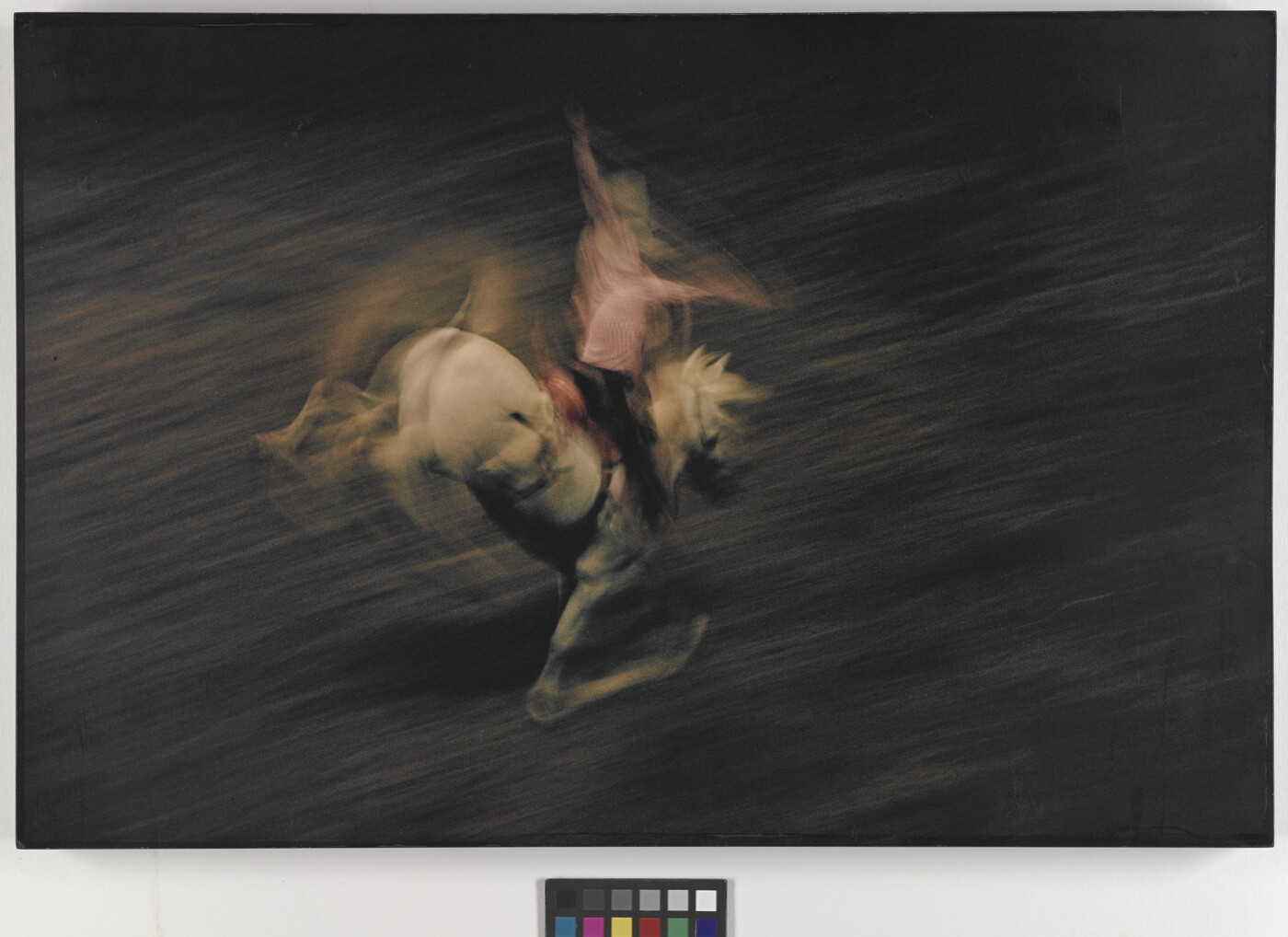 A color photograph of a cowboy on a bucking white horse, with the horse and cowboy blurred, indicating motion.
