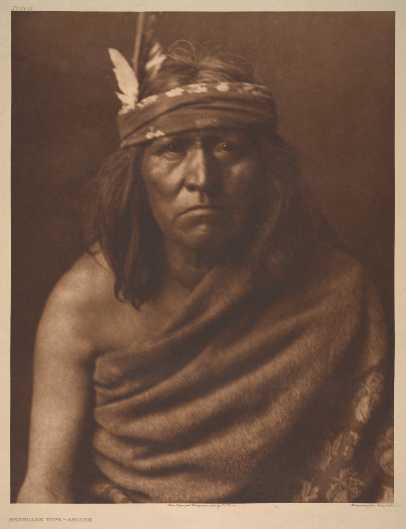 A sepia-toned portrait photograph of an Indigenous man with medium-length hair and a cloth around his forehead and cloth wrapped over one shoulder and around his torso.