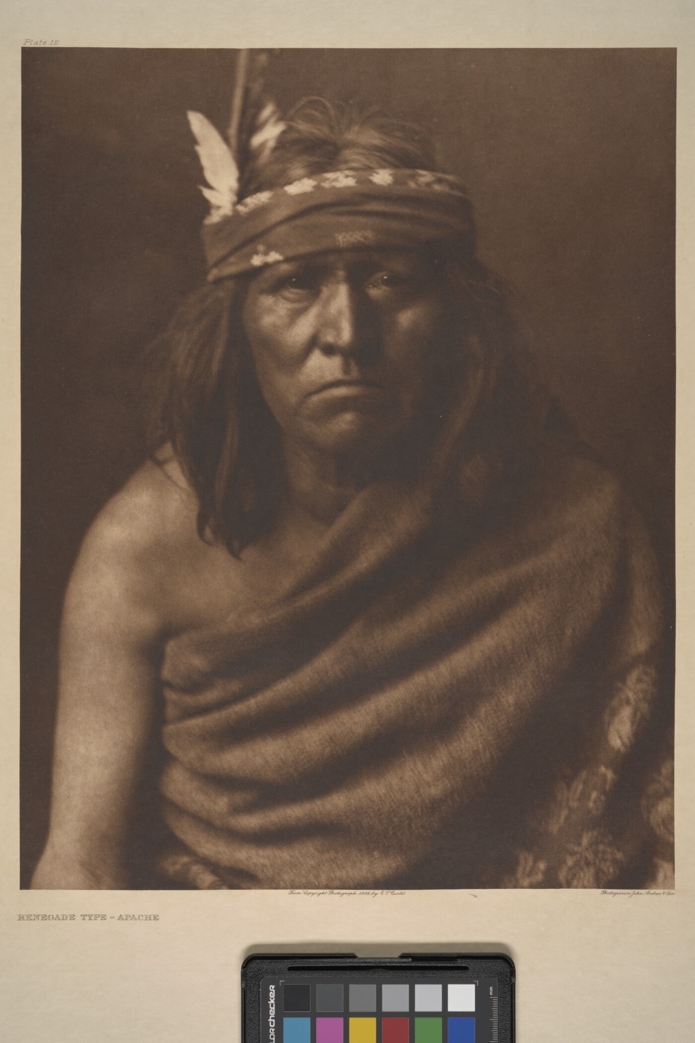 A sepia-toned portrait photograph of an Indigenous man with medium-length hair and a cloth around his forehead and cloth wrapped over one shoulder and around his torso.