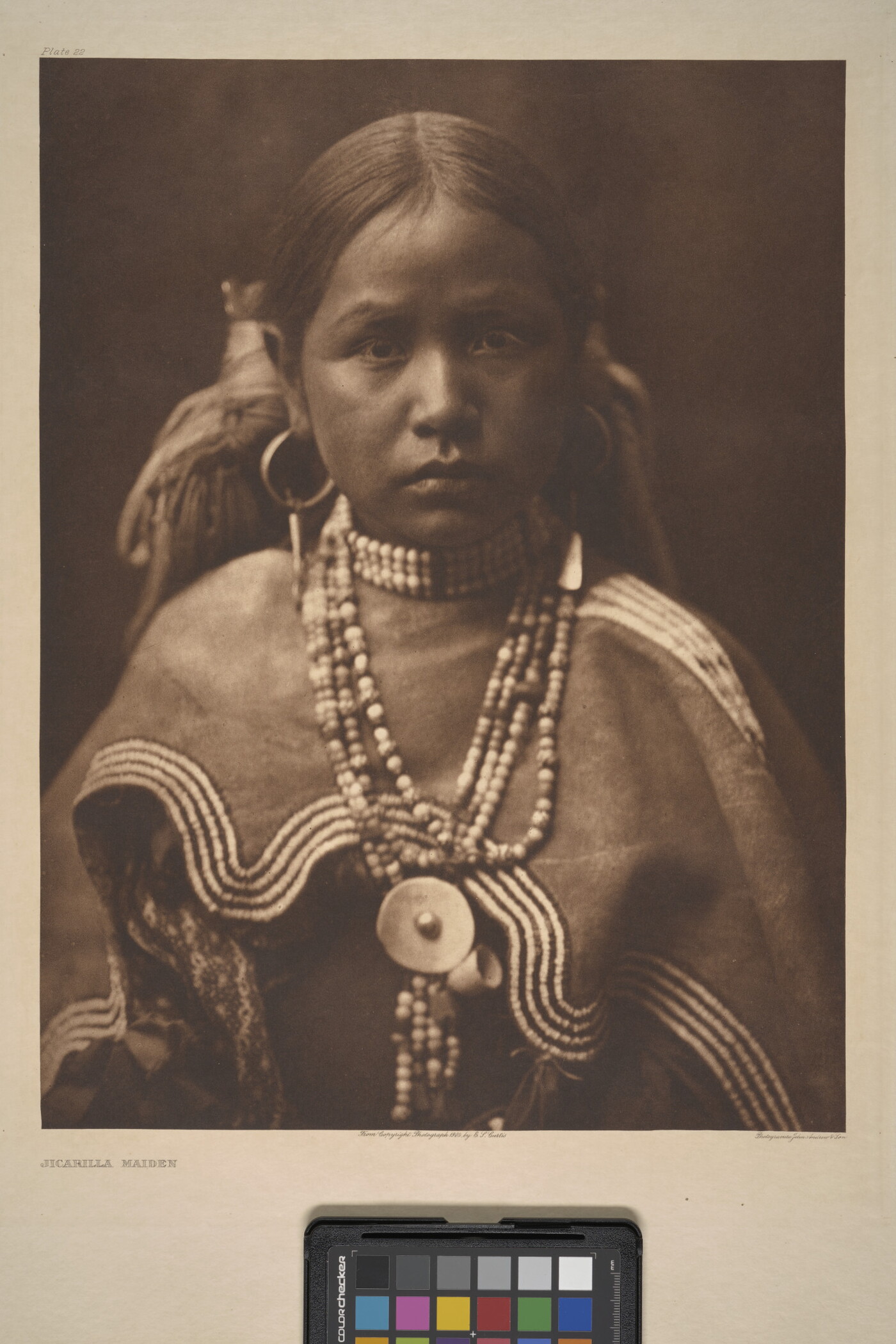 A sepia-toned portrait photograph of a young, Indigenous girl wearing a beaded necklace and cultural dress.