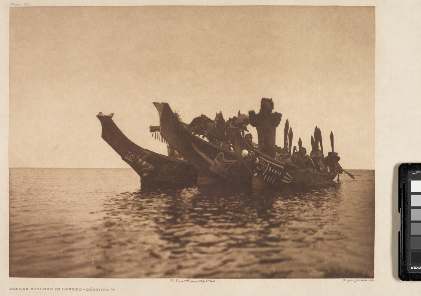 A sepia-toned photograph of three elaborately carved canoes side-by-side on a body of water with several masked Indigenous people in each canoe.