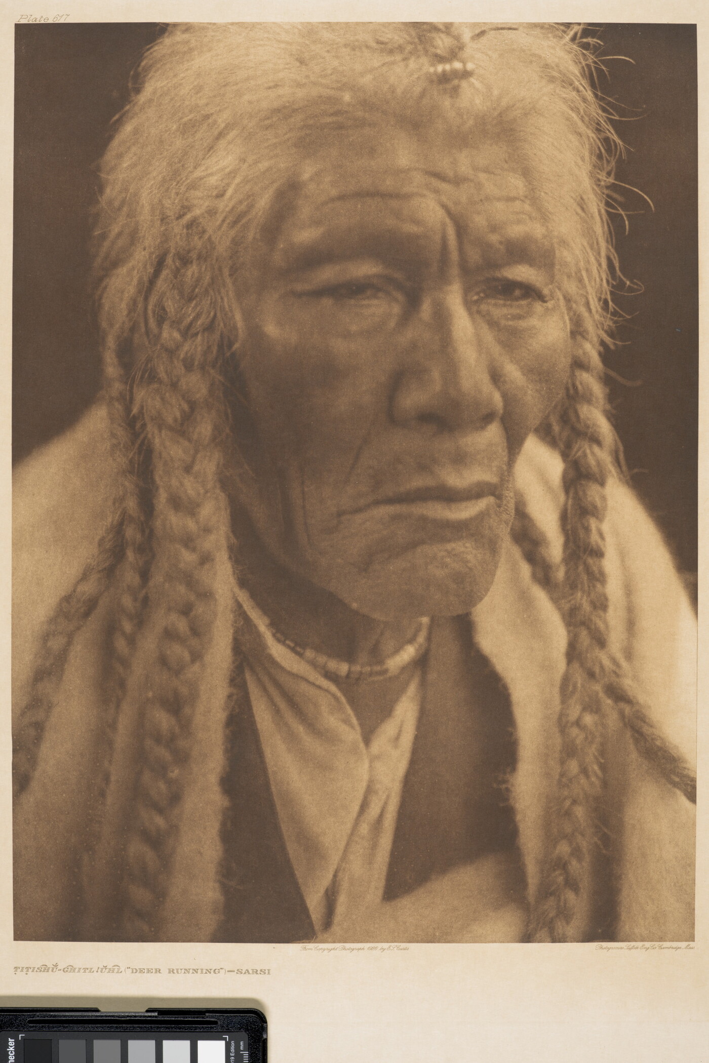 A sepia-toned portrait photograph of an elderly Native American man with long, gray hair in several braids gazing out.