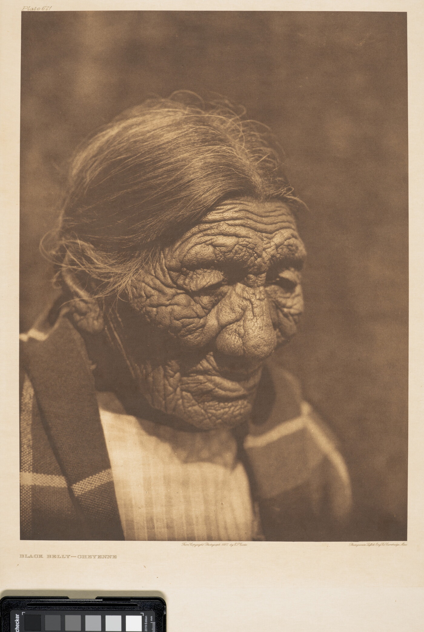 A sepia-toned photograph of an elderly Indigenous person with hair pulled back and a blanket around their shoulders.
