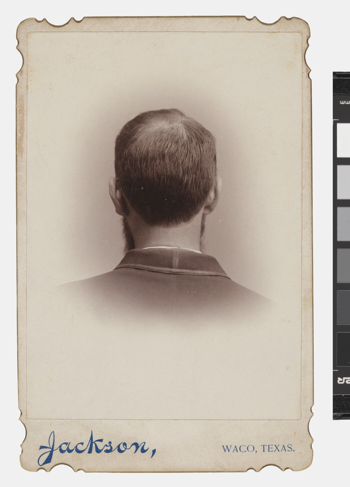 A black-and-white studio portrait photograph of the back of the head, from the neck up, of a man with short hair.