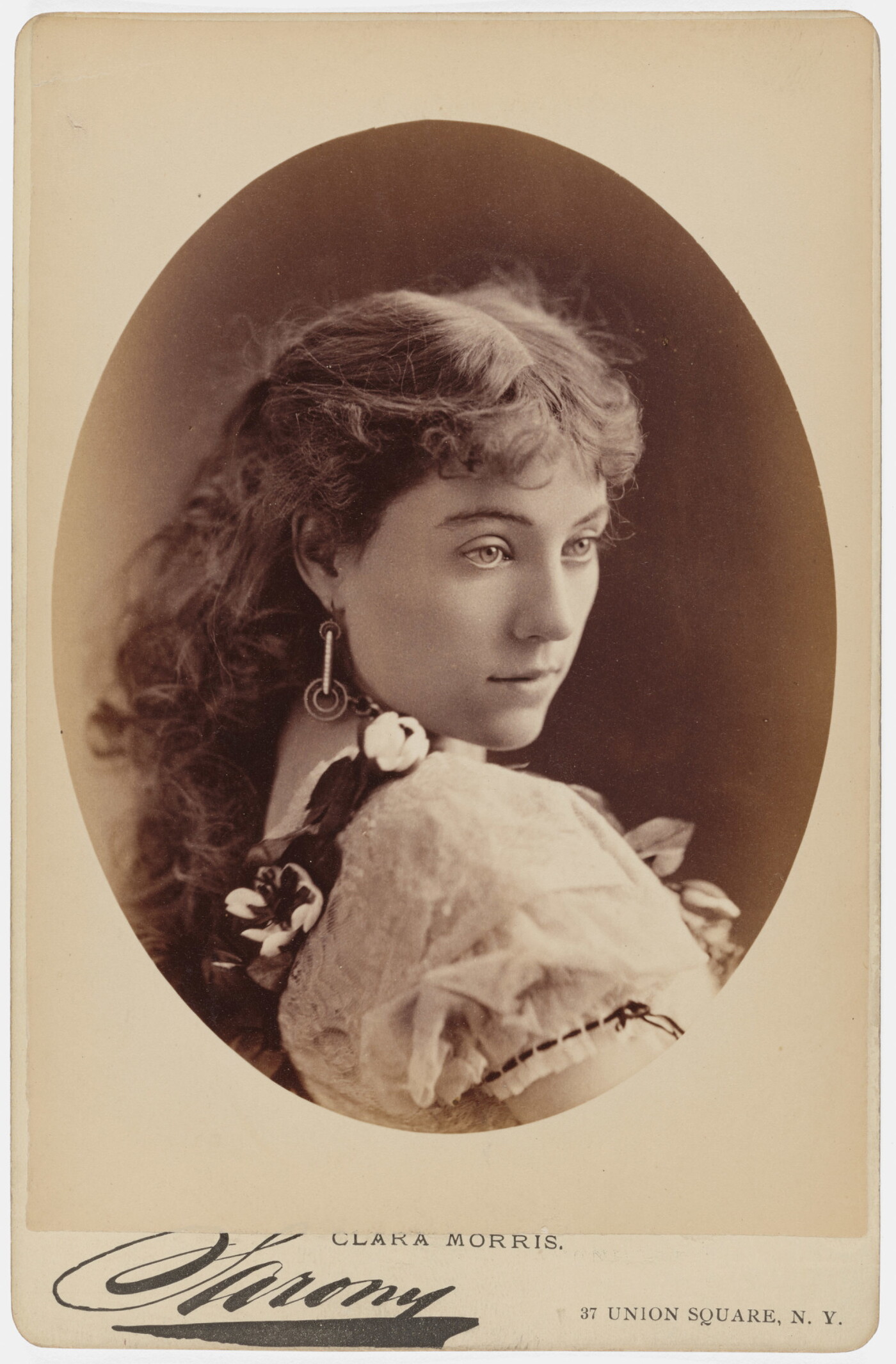 A sepia-toned studio portrait photograph of a young White woman gazing over her shoulder.