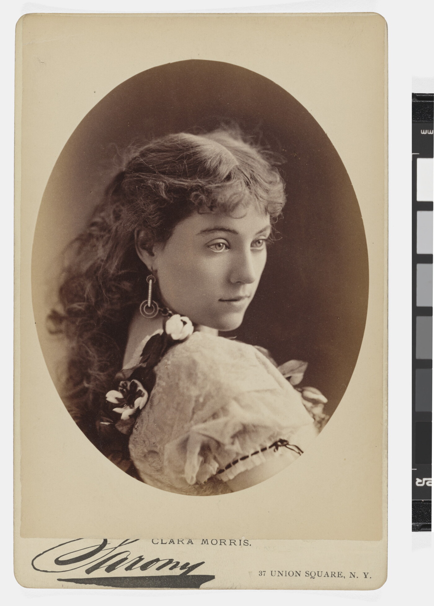 A sepia-toned studio portrait photograph of a young White woman gazing over her shoulder.