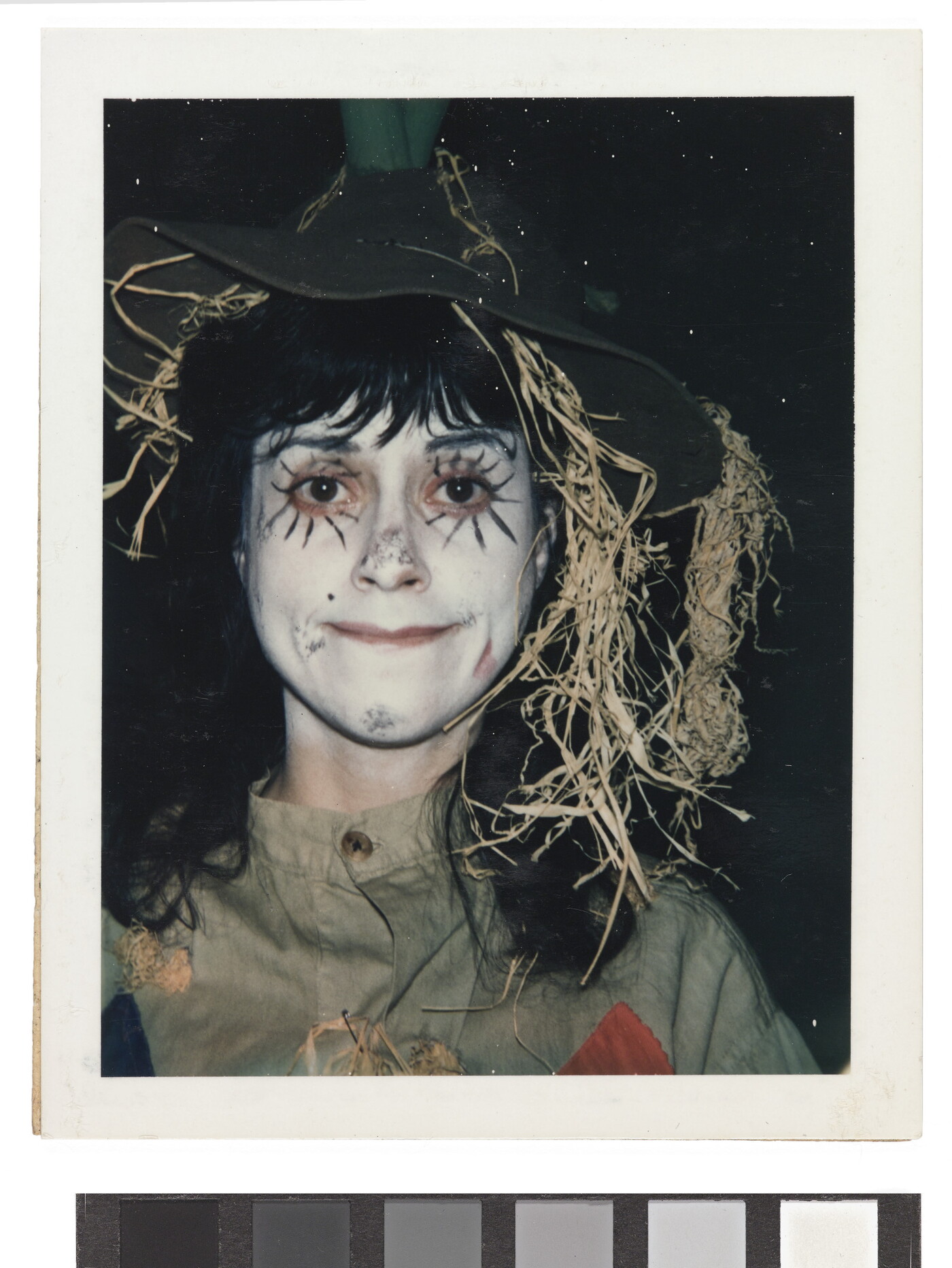 A color portrait of a girl wearing white face paint and dressed as a scarecrow.